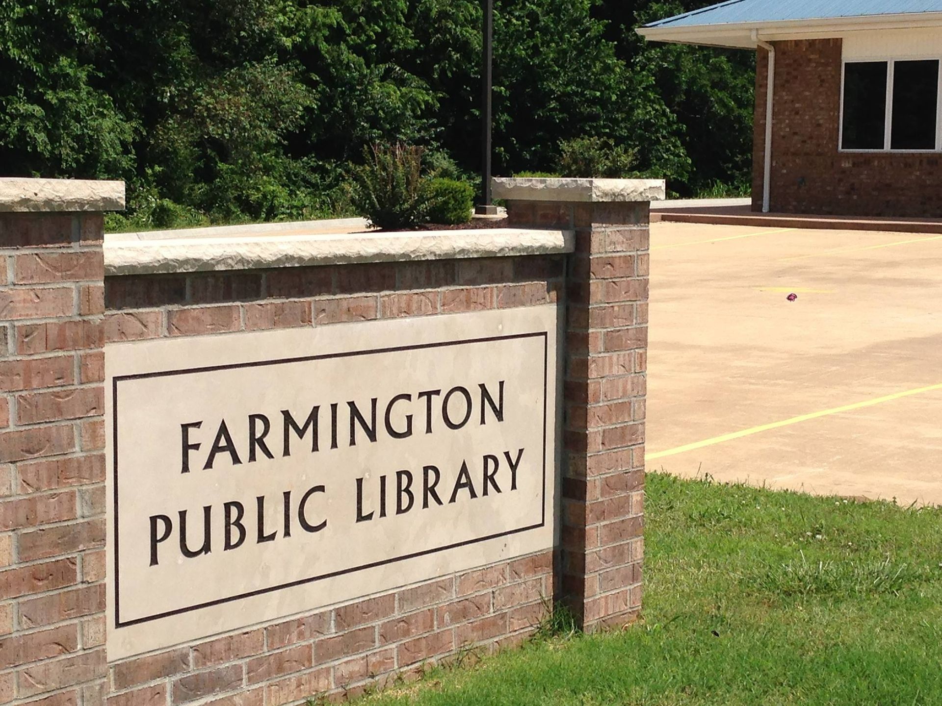 Sign for Farmington Public Library, brick structure, with building in the background.