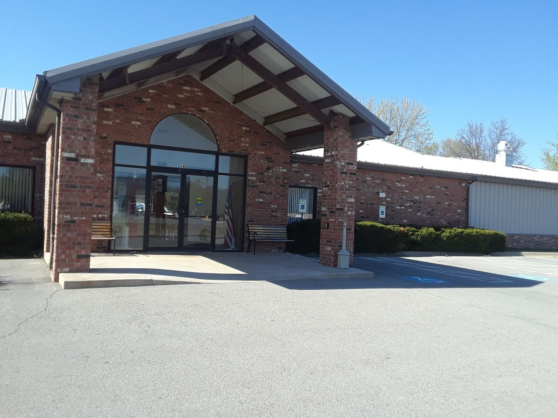 Brick building with a glass entrance under a covered area. A small bench sits outside.