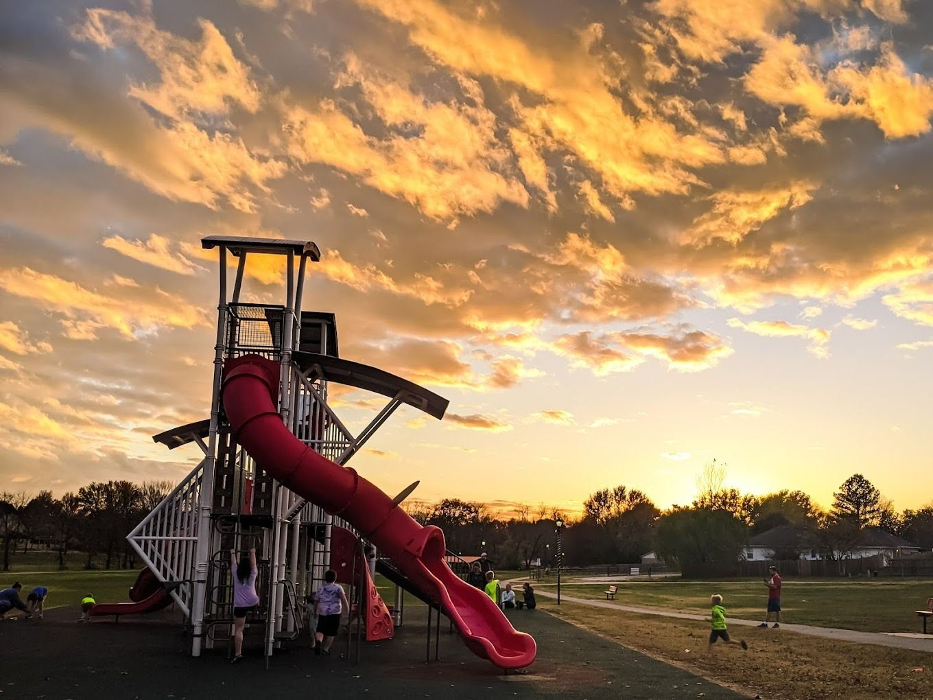 Playground with red slide, children, and vibrant sunset sky.