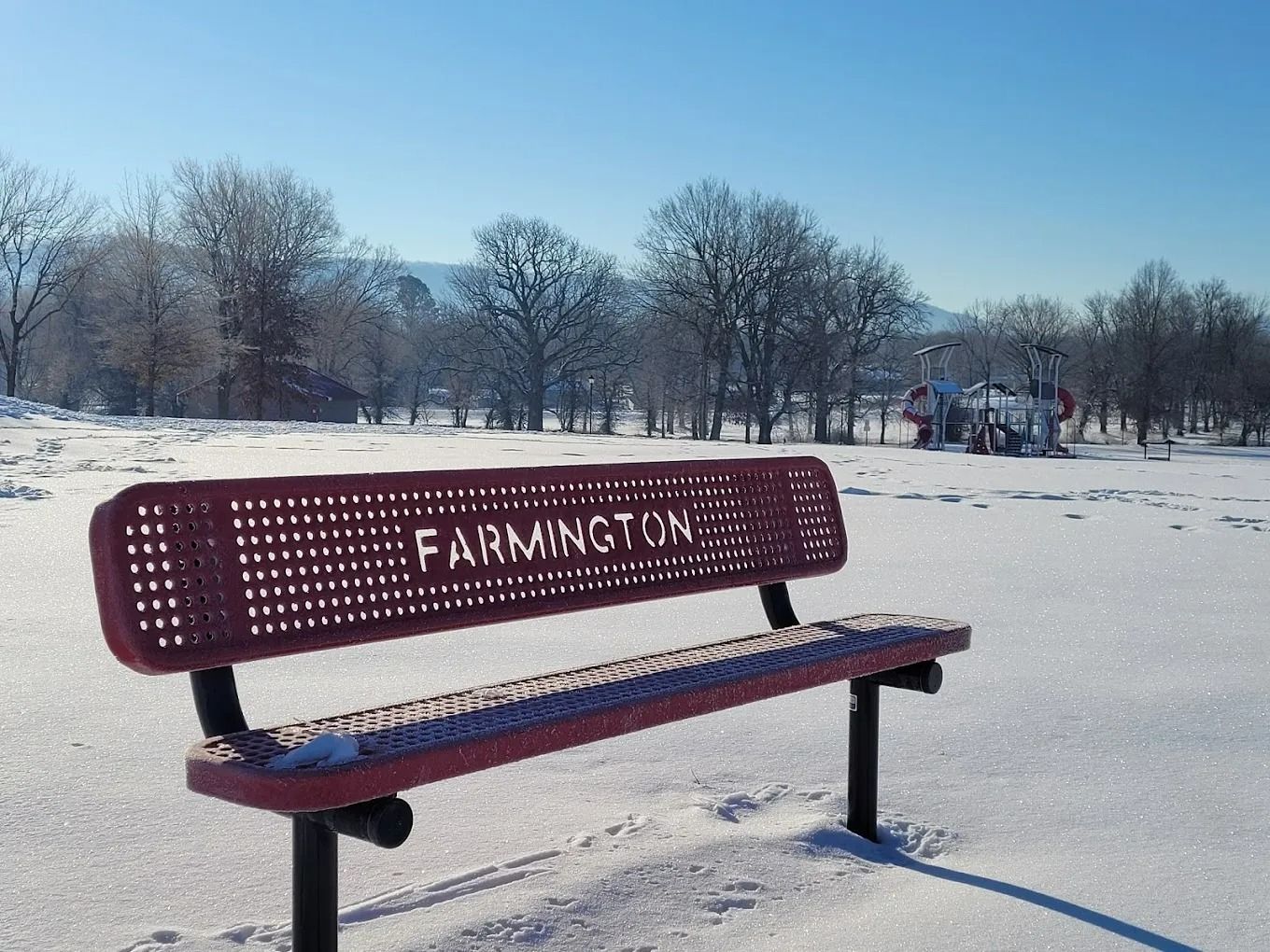 Red bench in Farmington park covered in snow, sunny winter day.