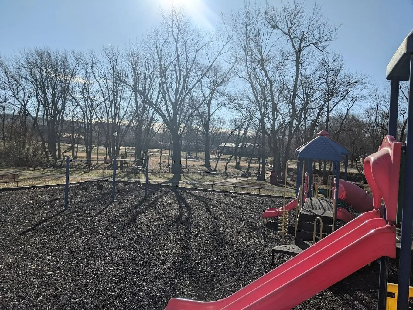 Playground with red slide, trees in background, sunny day.