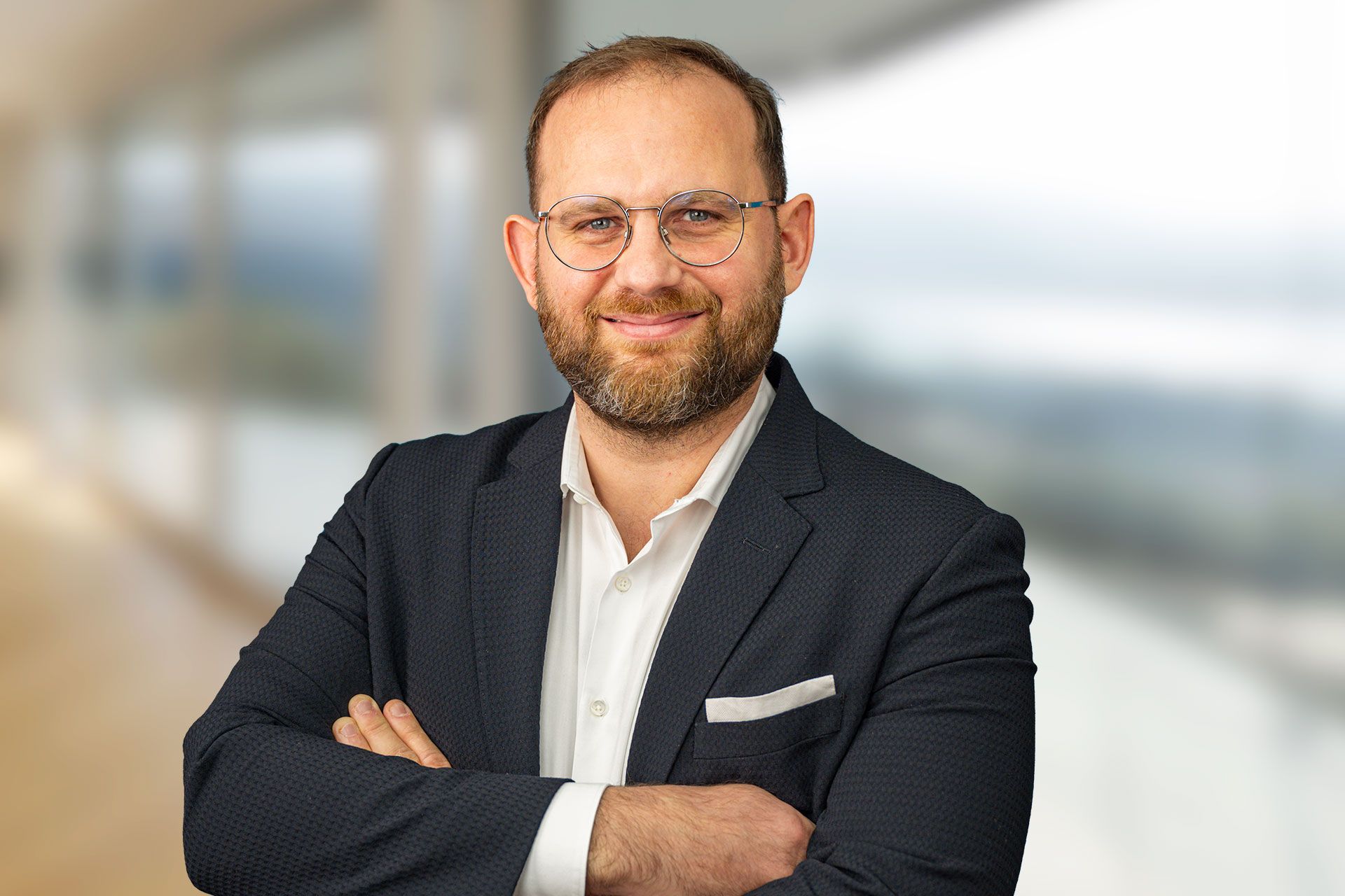 A man in a suit and glasses stands with his arms folded.