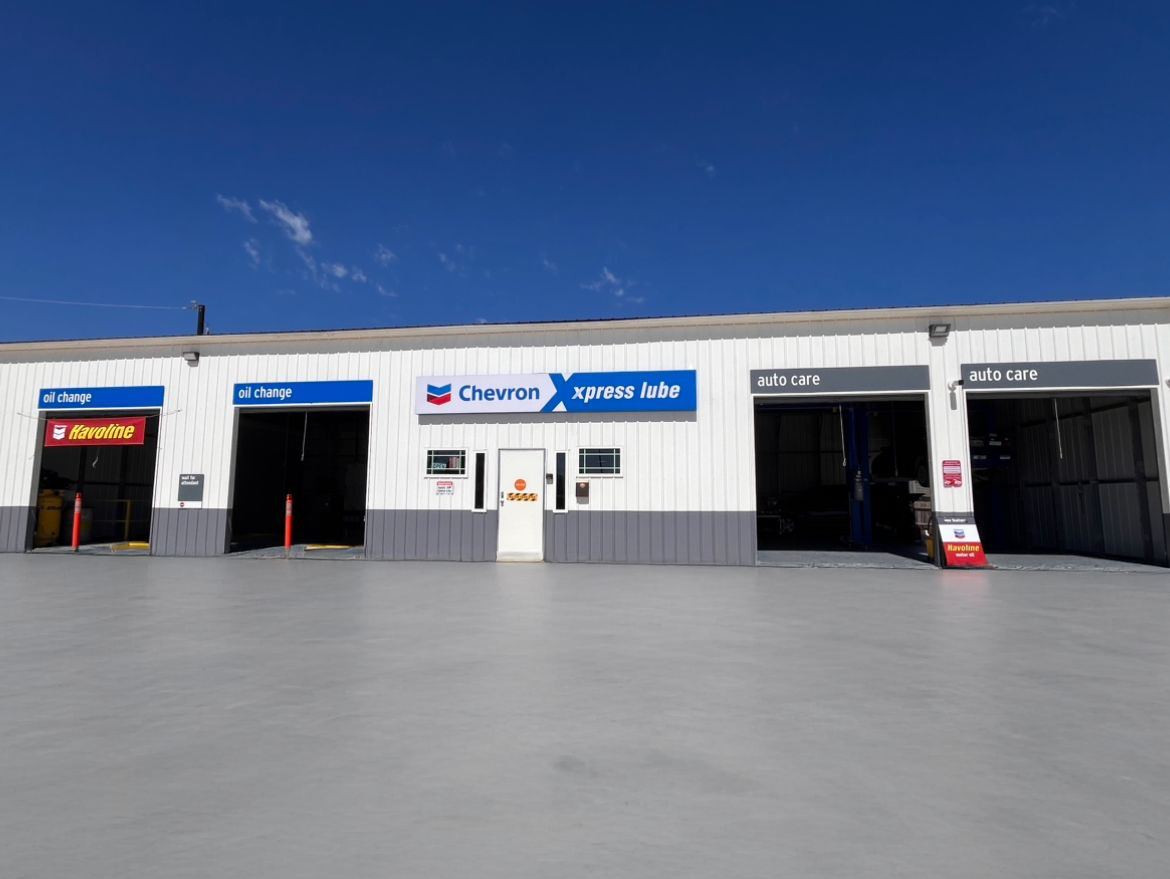 Exterior view of an auto repair shop with bays, white building, blue sky, signage.