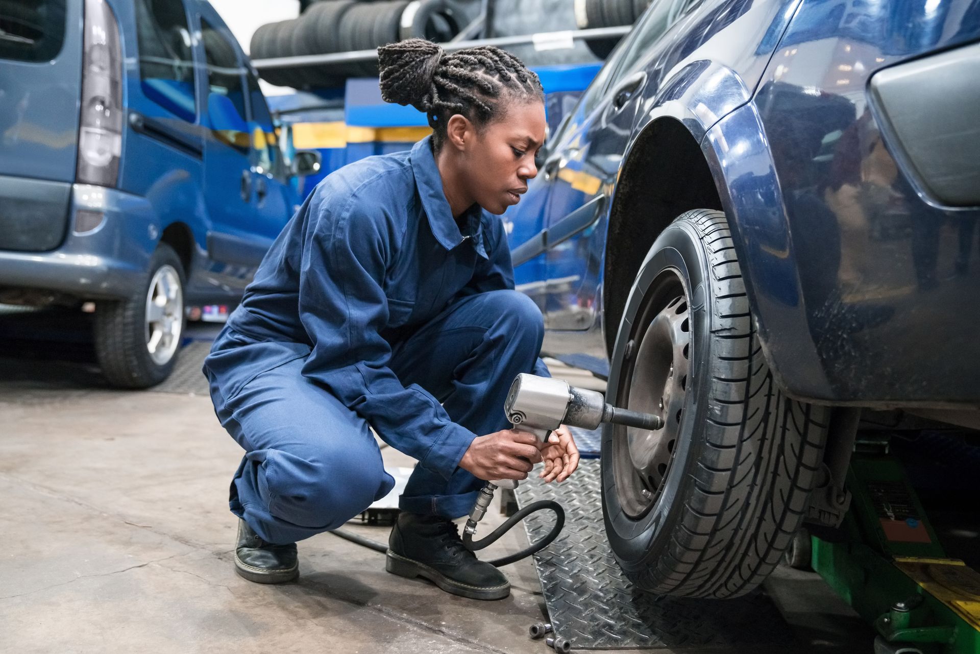 Mechanic in blue uniform tightening lug nuts on a car tire with a wrench.
