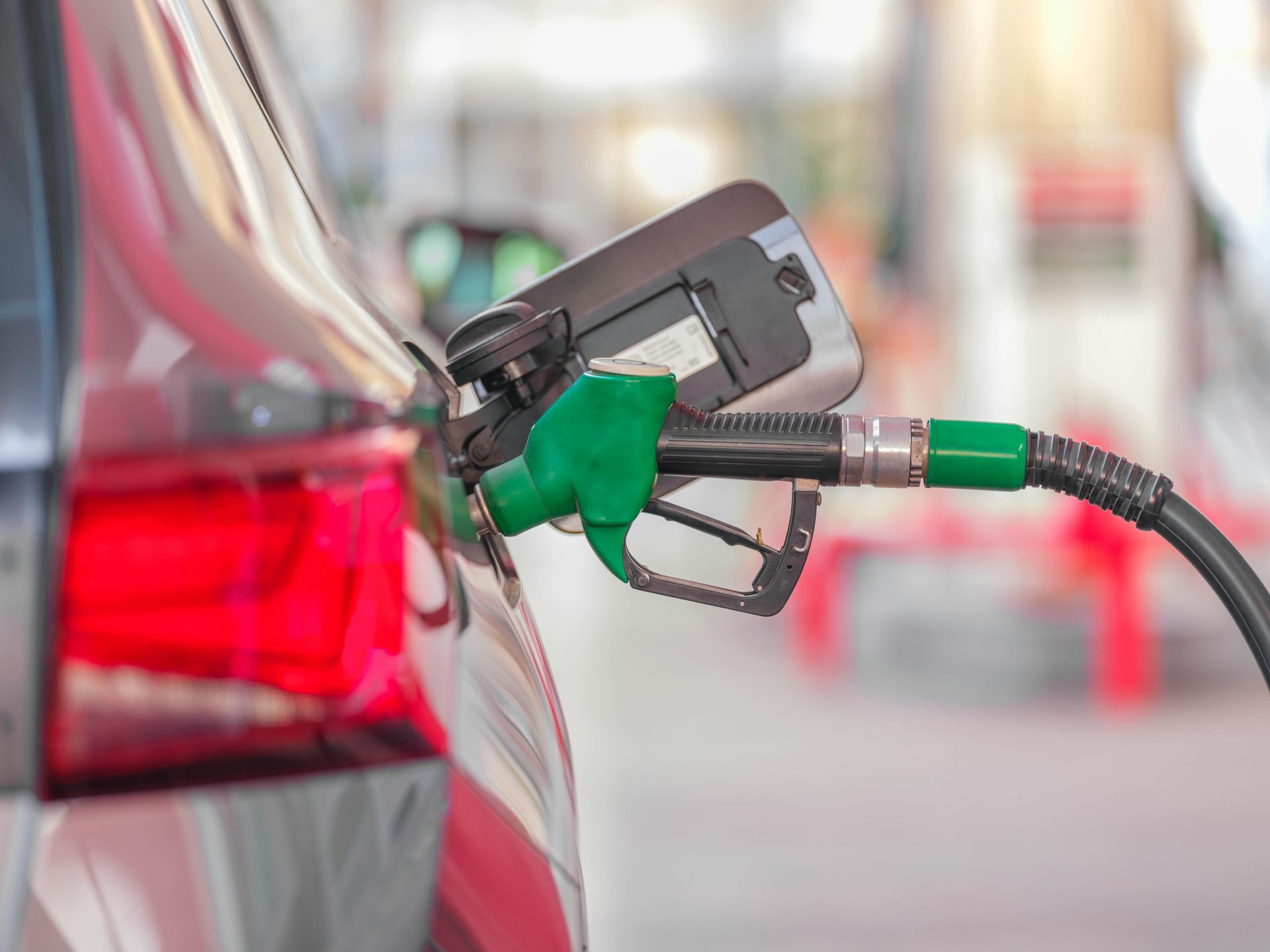 A car being fueled at a gas station, with a green fuel nozzle inserted.