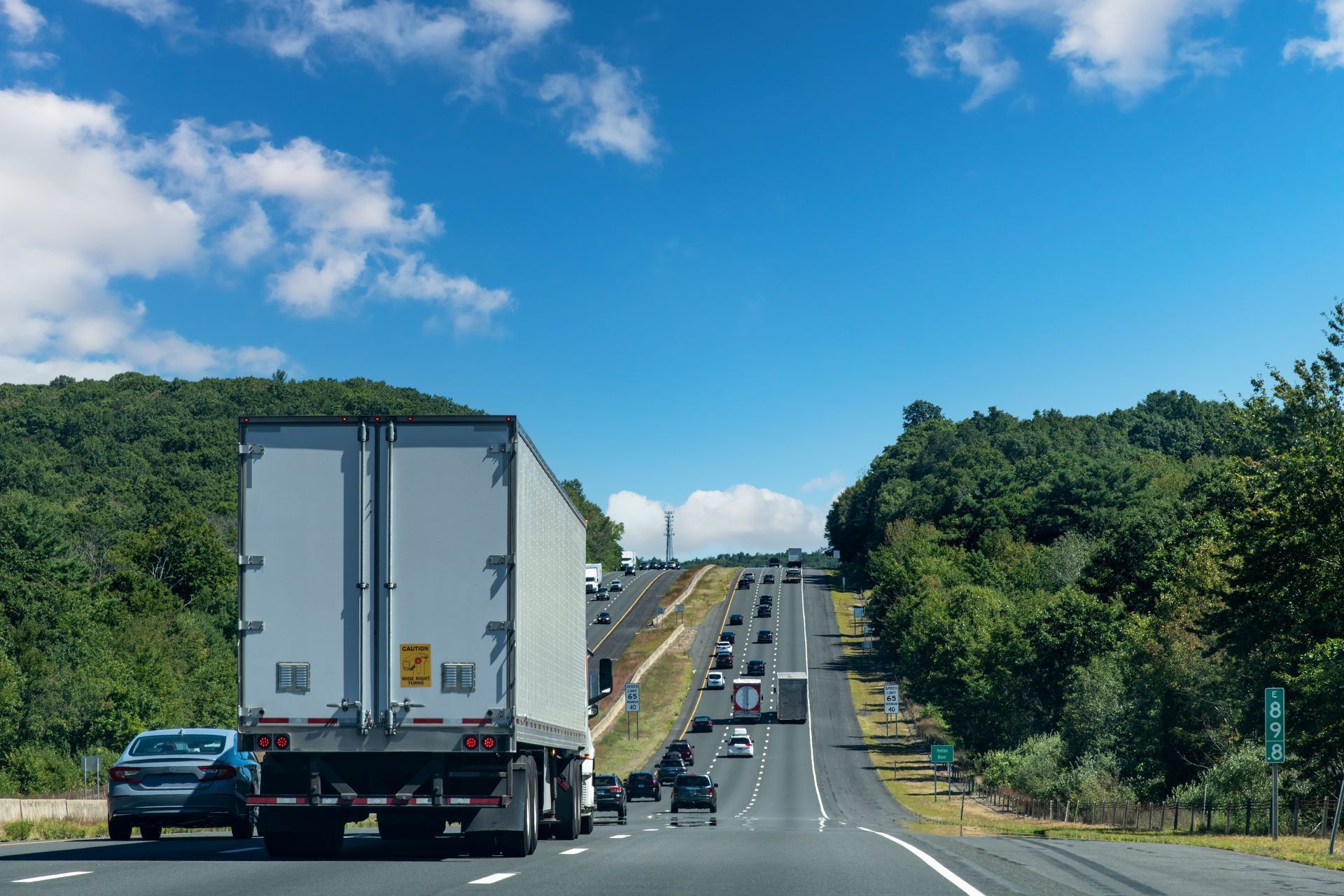 A semi truck is driving down a highway next to a forest.