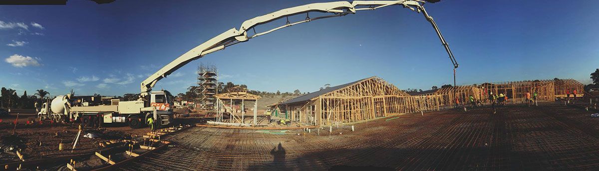 Construction site with a concrete pump truck pouring concrete onto a partially constructed building. Blue sky.