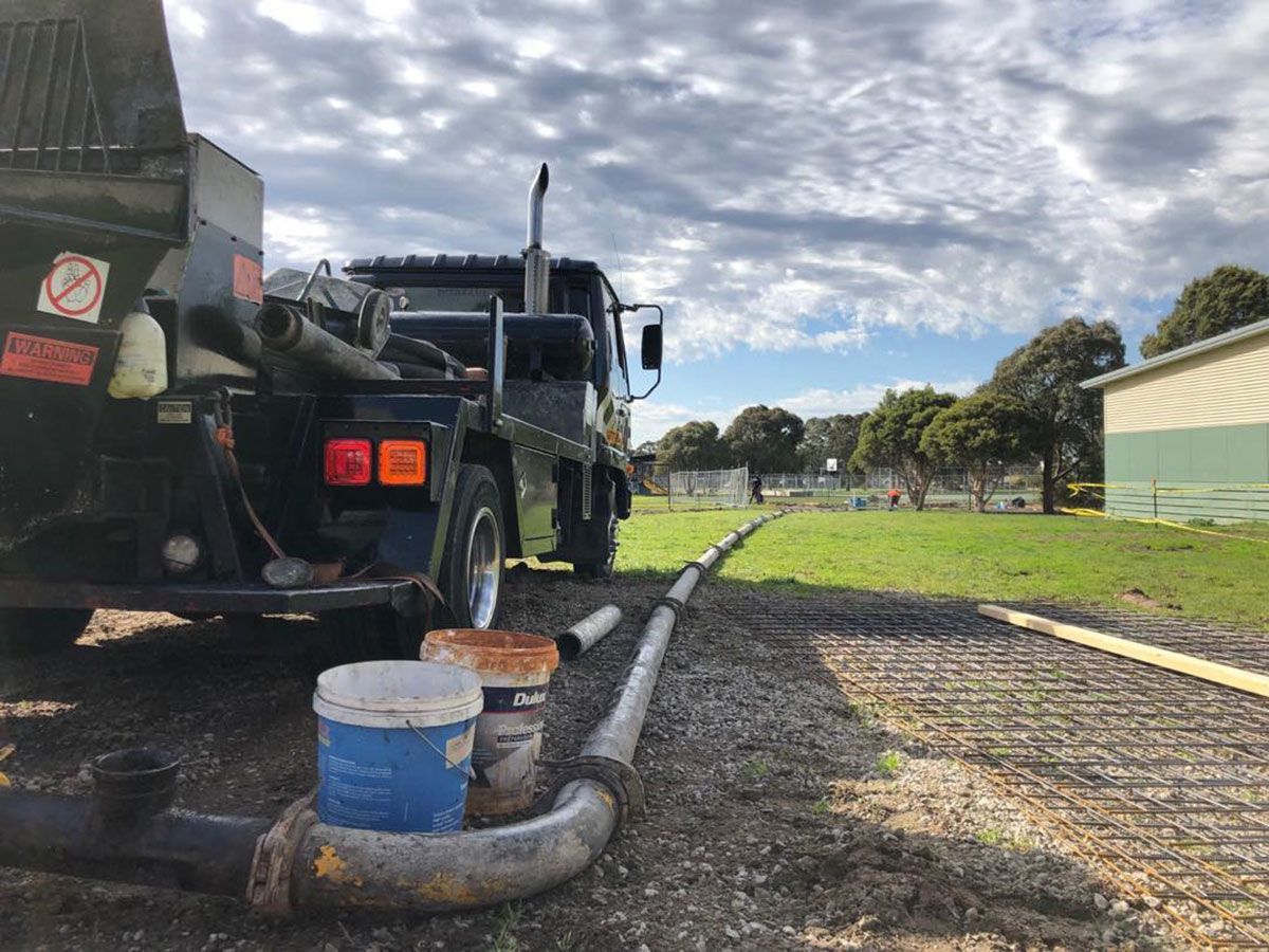 Concrete truck with a hose delivering concrete to a construction site on a grassy field.