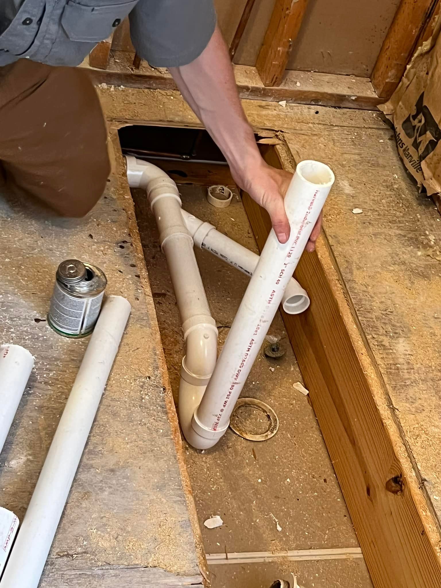 A person is holding a white pipe in a hole in the floor.