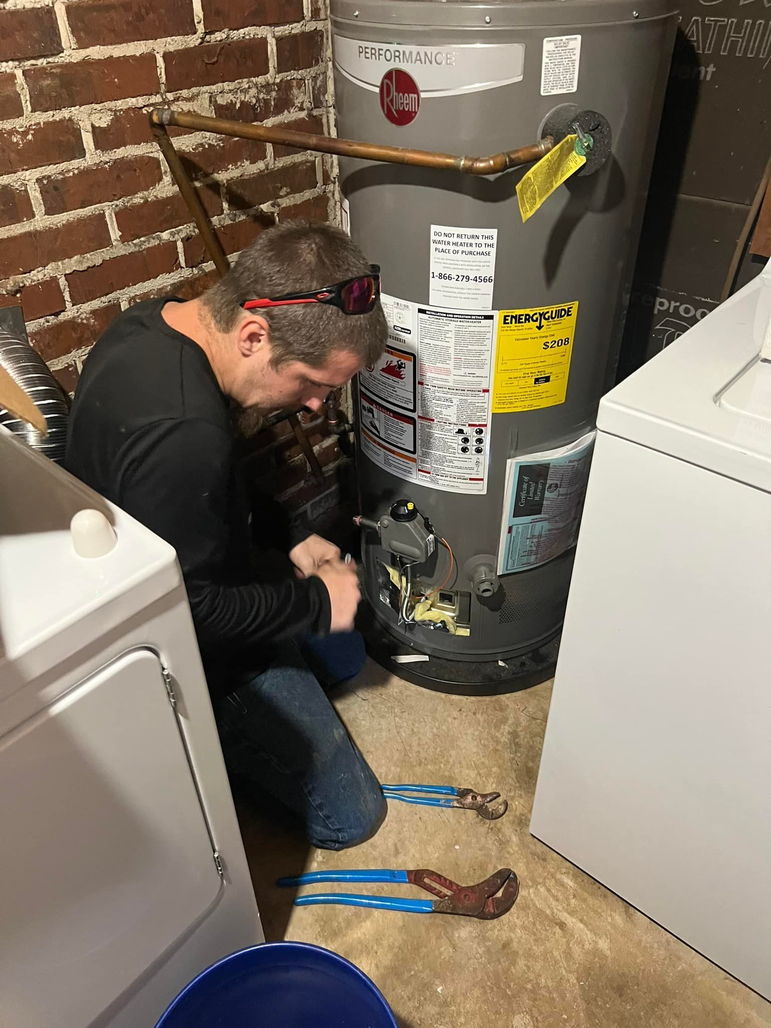 A man is working on a water heater in a laundry room.