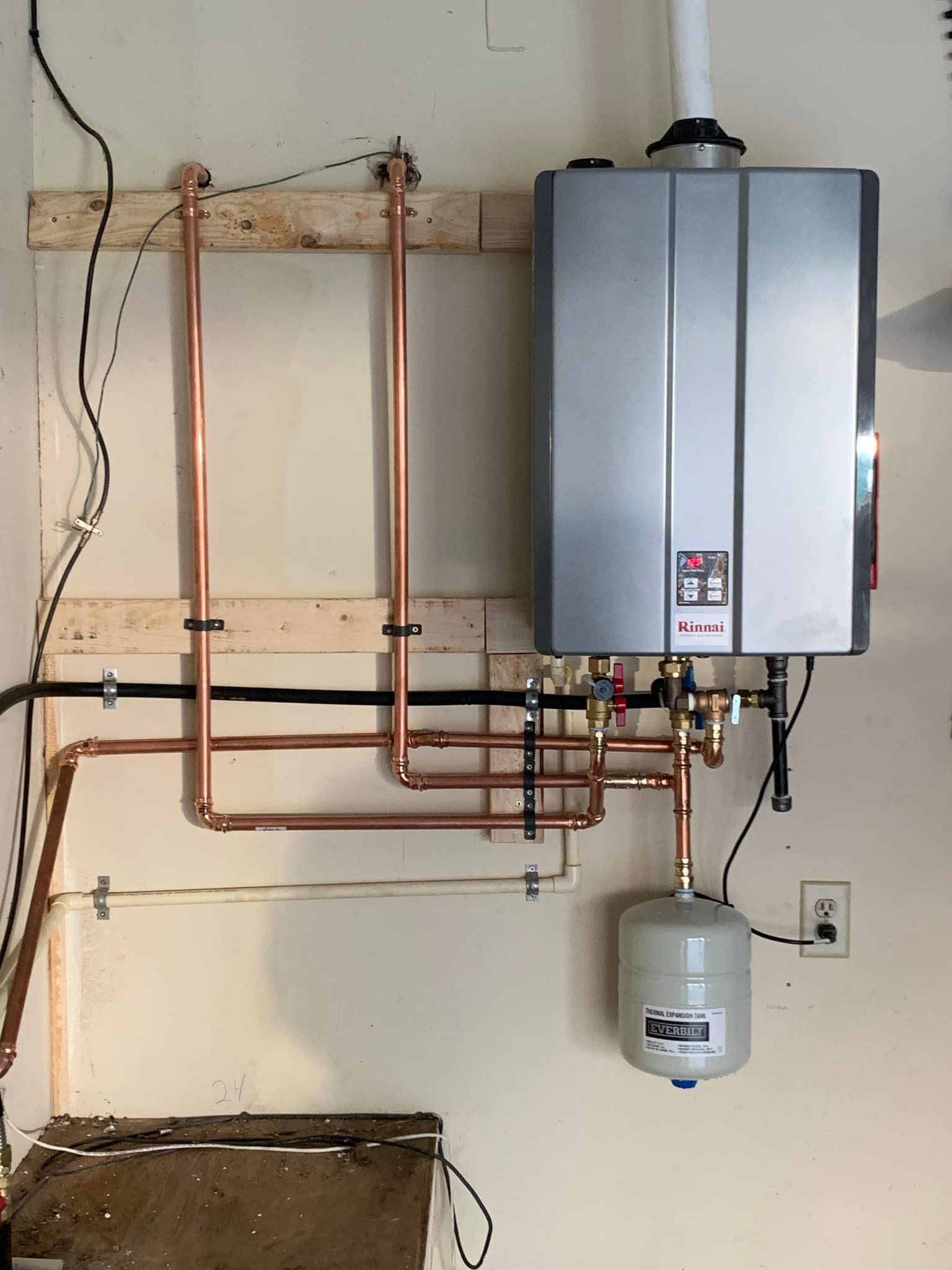 A water heater is hanging on a wall next to copper pipes.