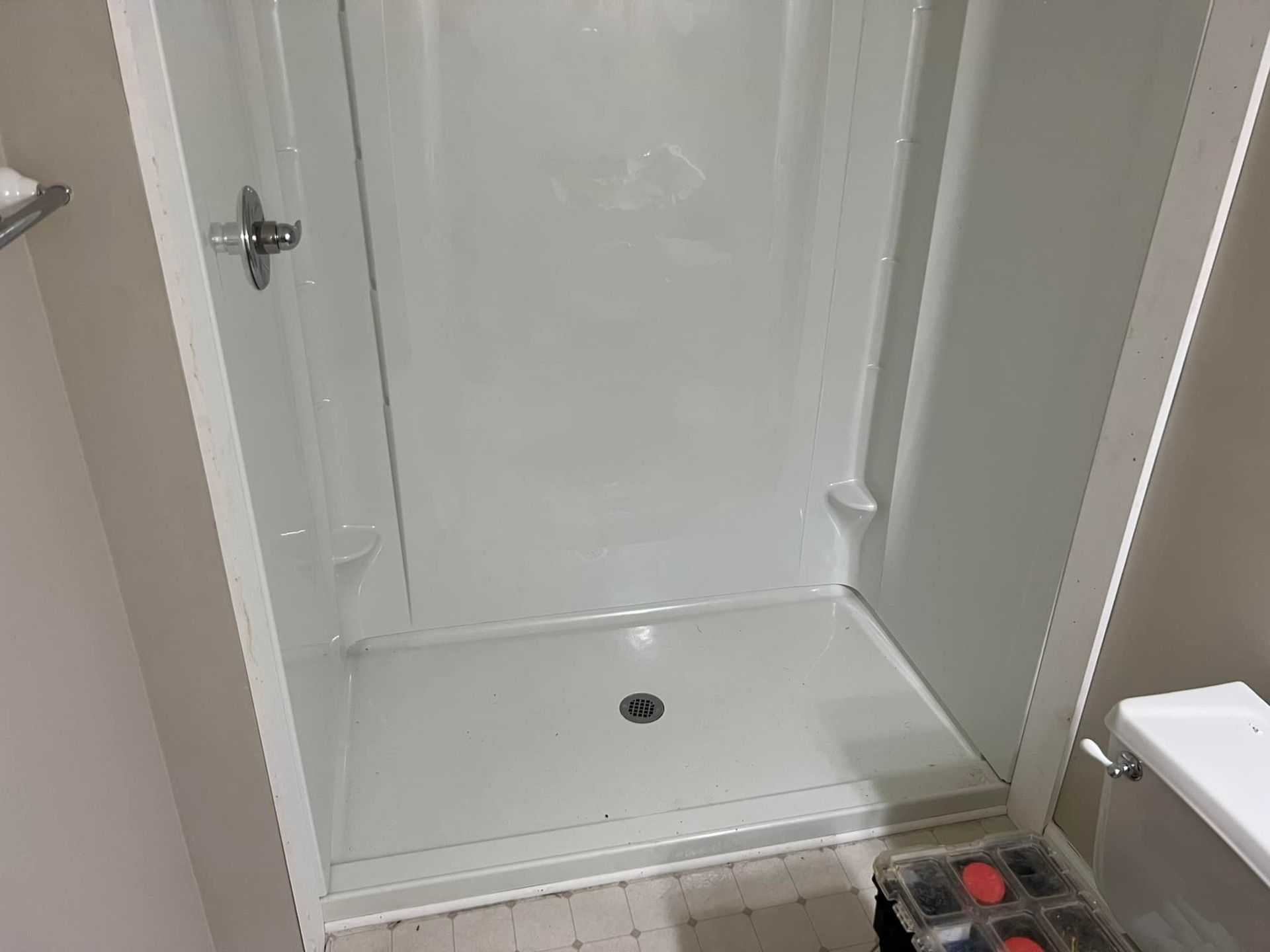 A white shower stall in a bathroom next to a toilet.