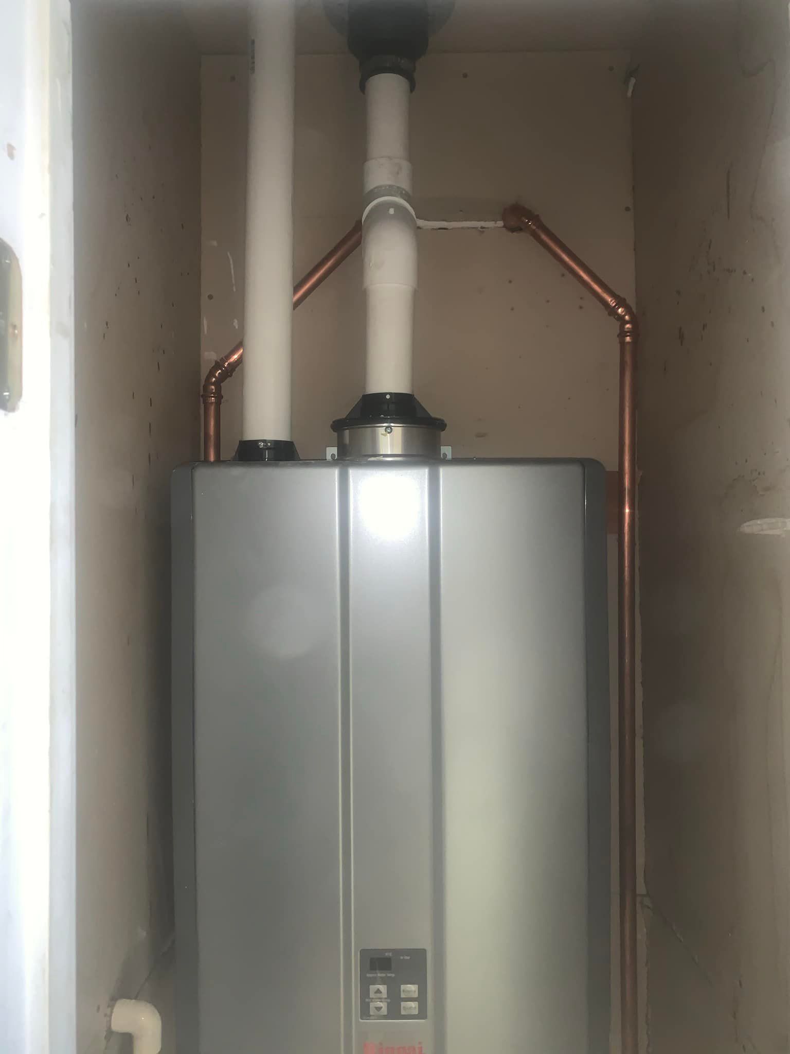 A water heater is sitting in a closet next to copper pipes.