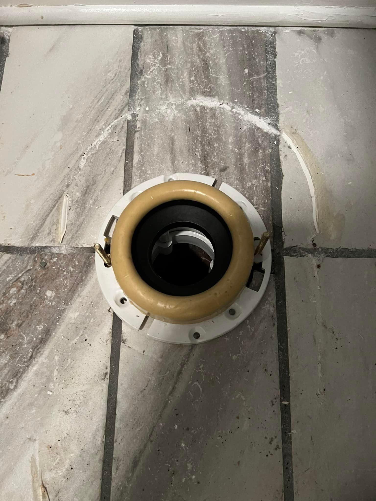 A close up of a toilet flange on a tiled floor.
