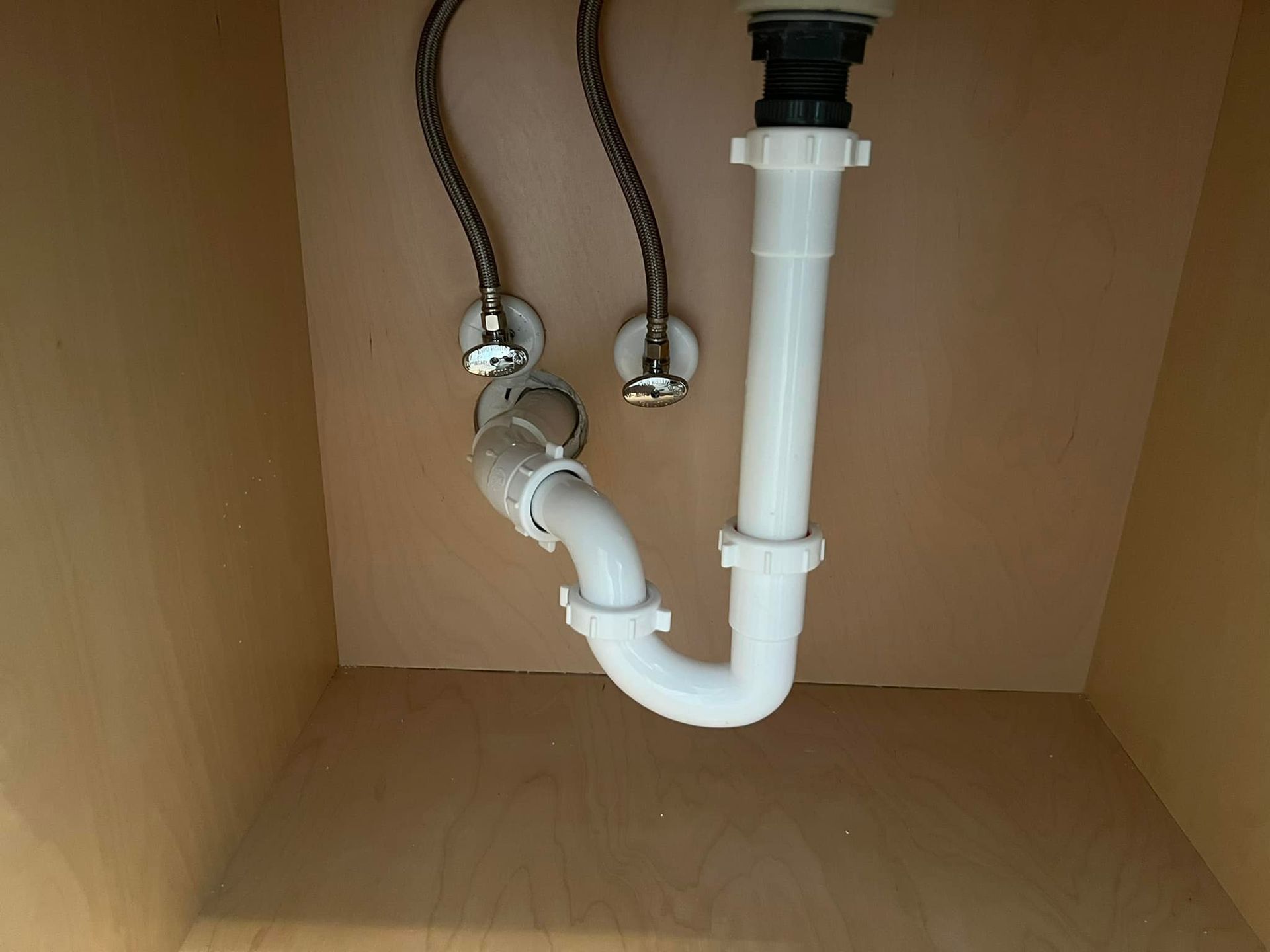 A white pipe is connected to a sink in a cabinet.
