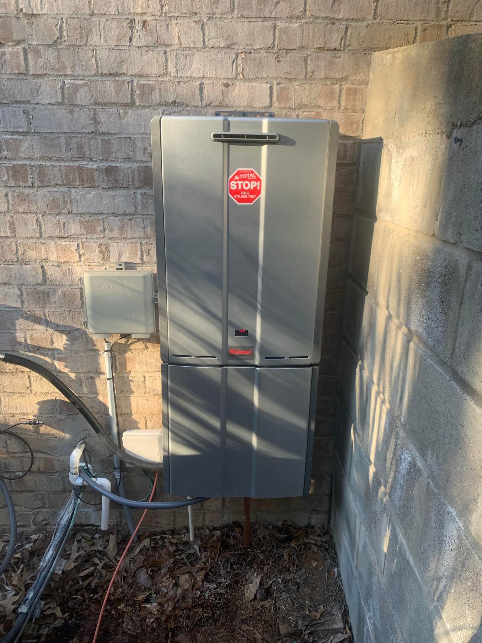A gray water heater is attached to a brick wall.