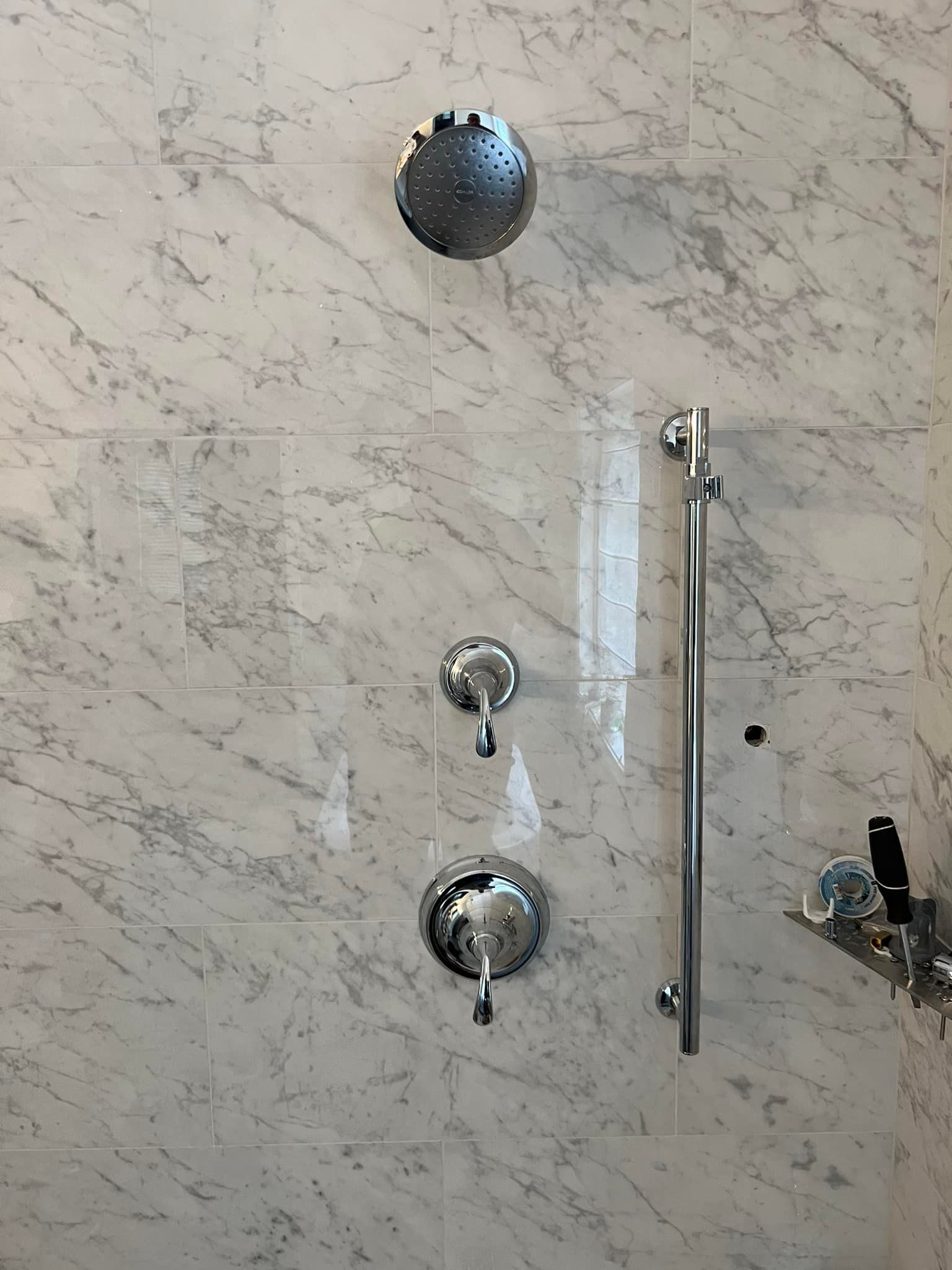 A shower with a marble wall and a chrome shower head.