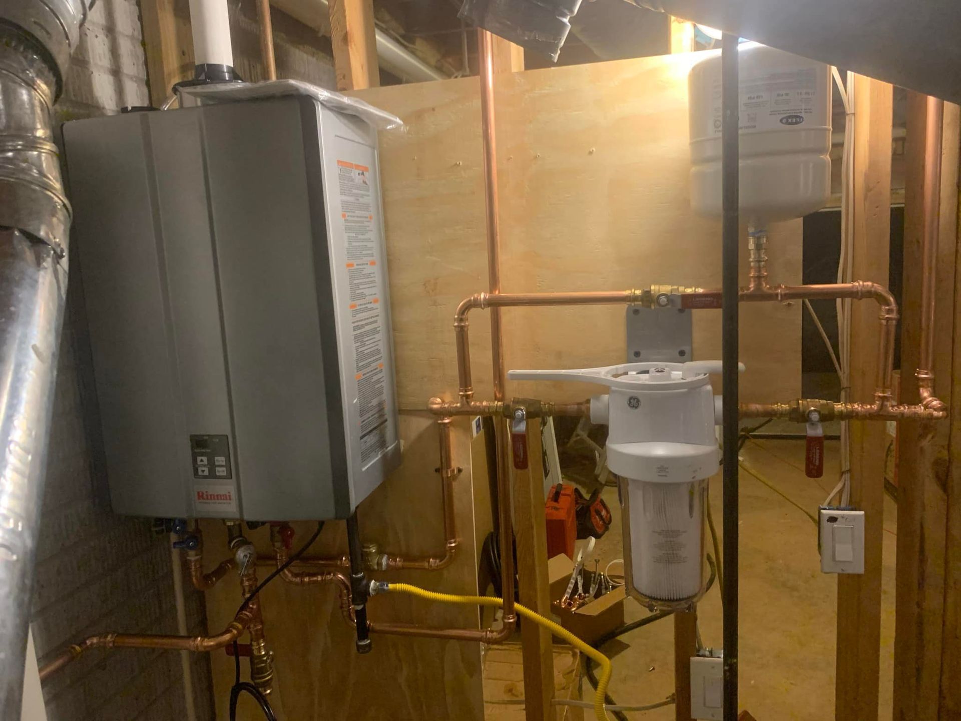 A water heater is sitting in a room with copper pipes.