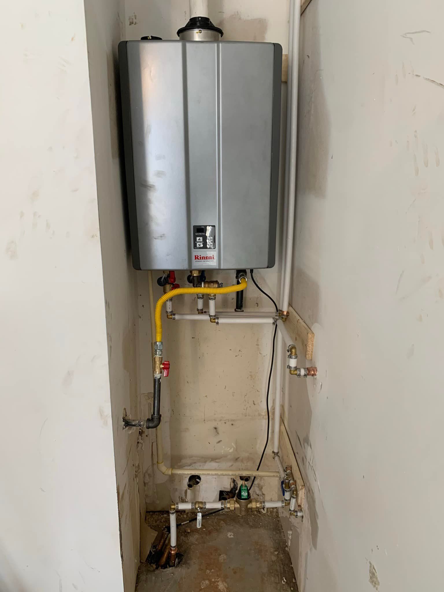 A water heater is sitting in a corner of a room next to a wall.