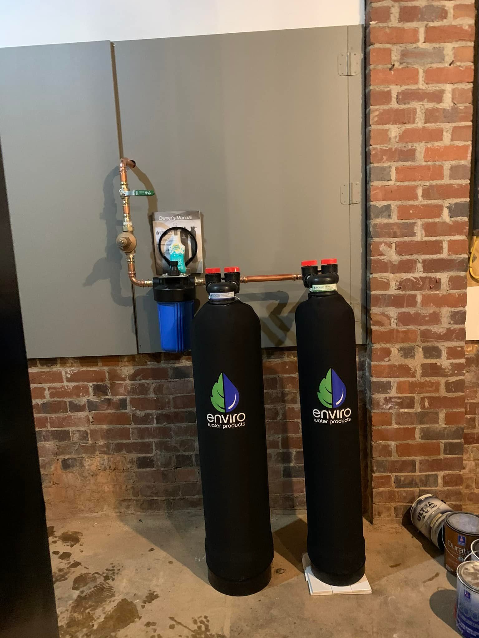 Two water filters are sitting next to each other in a room next to a brick wall.