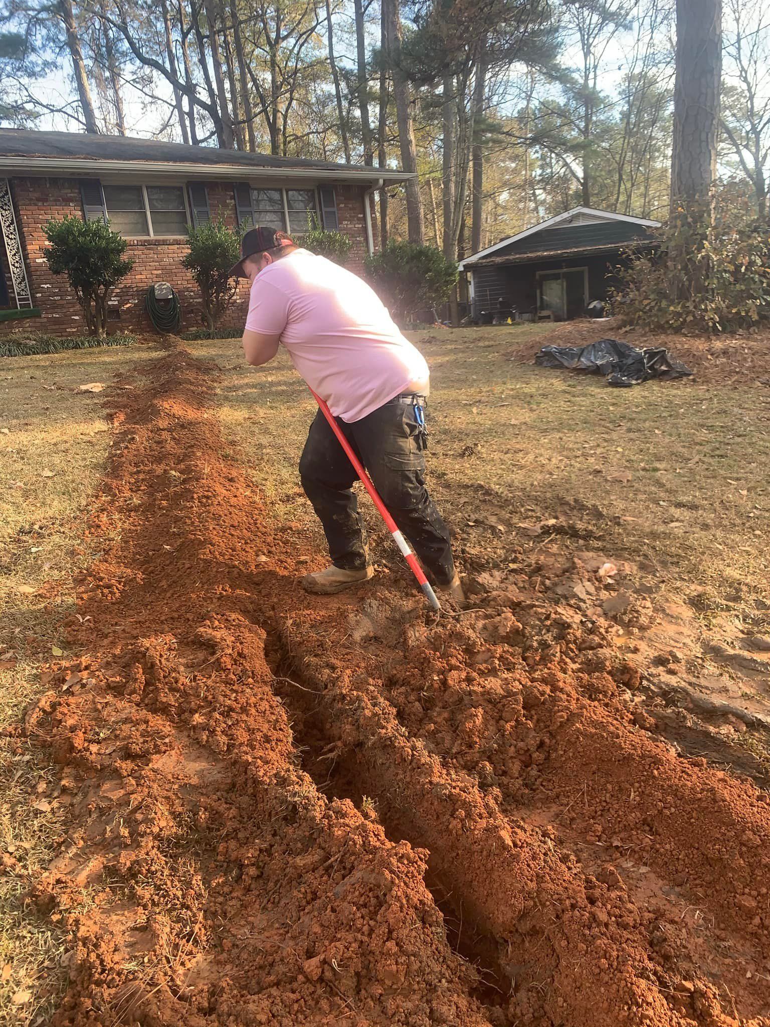 A man is digging a trench in the dirt in front of a house.