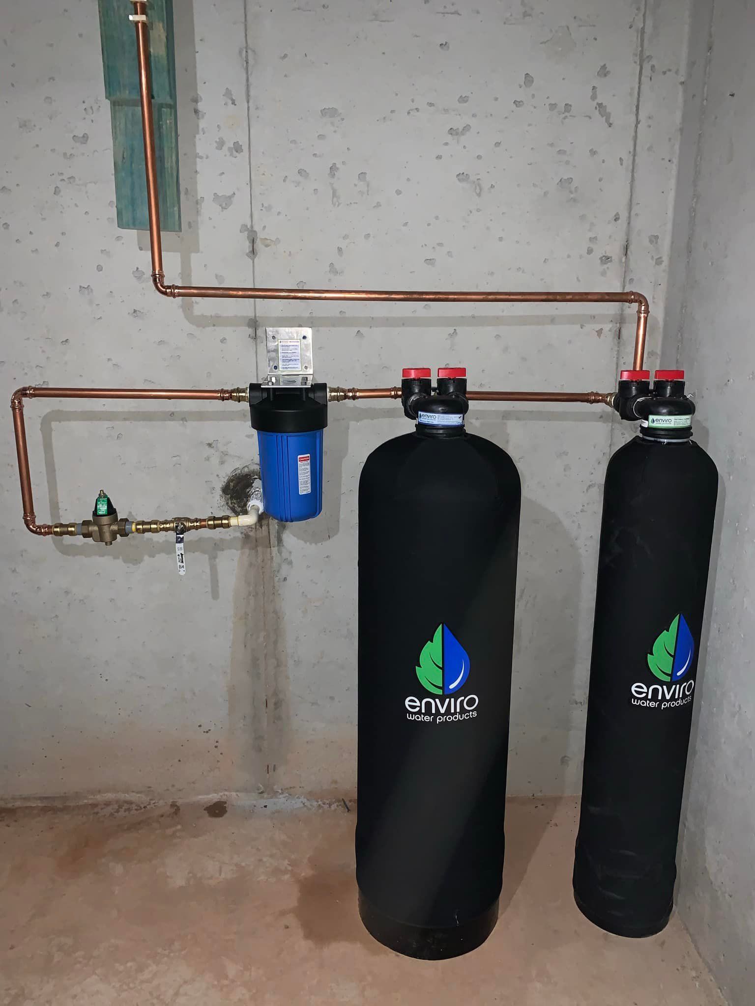 Two water filters are connected to a copper pipe in a basement.