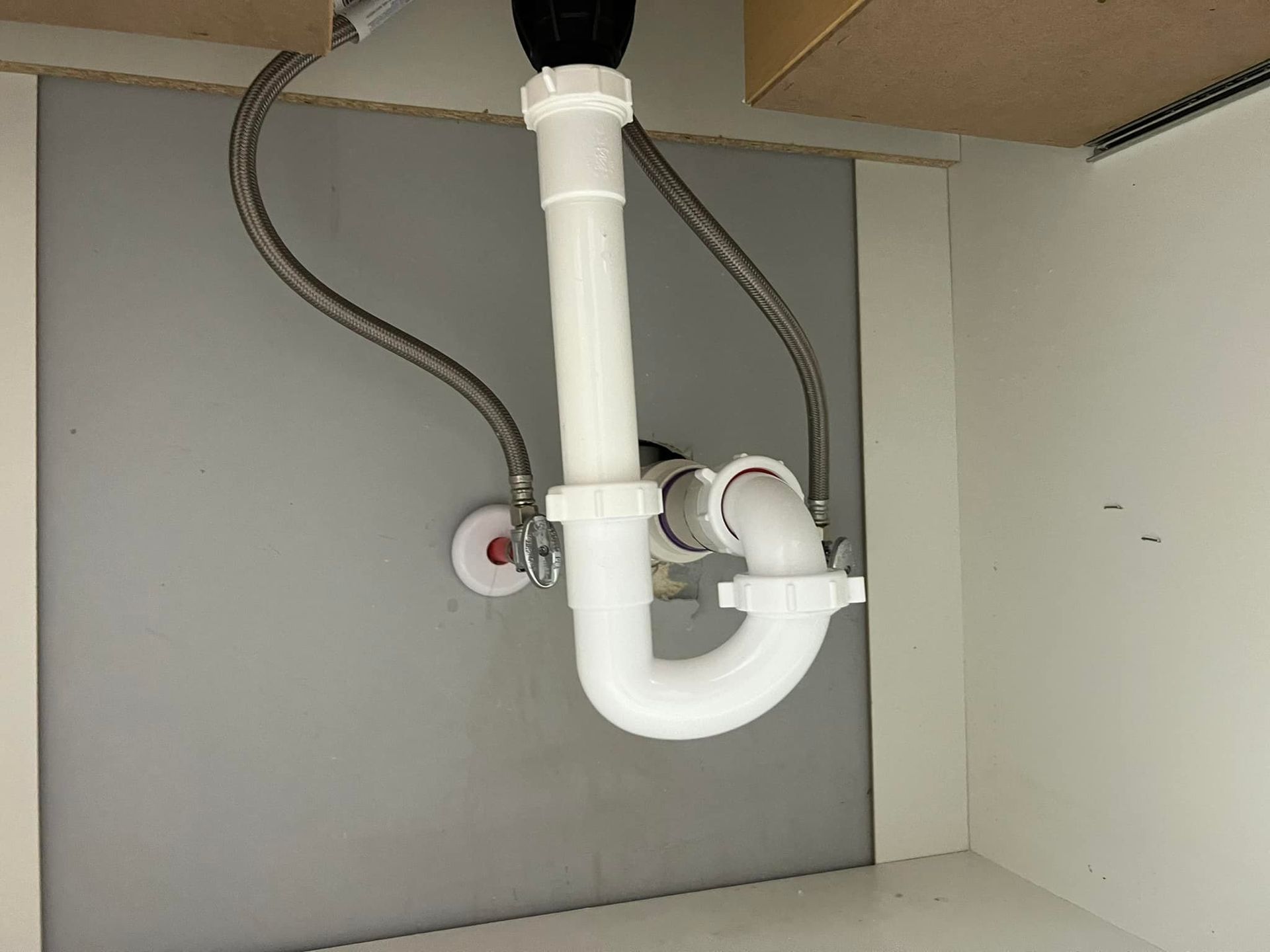 A white plumbing pipe is hanging from the ceiling under a sink.