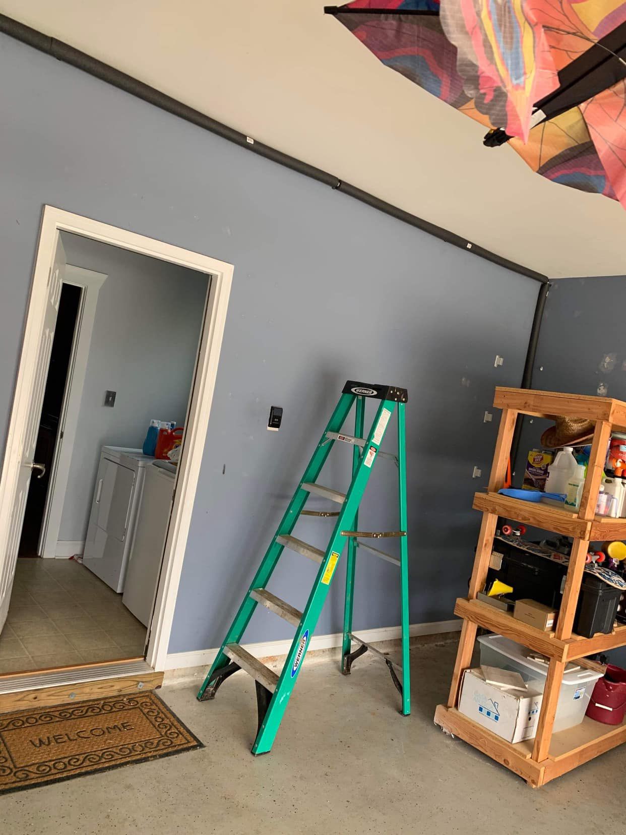 A green ladder is sitting in a room next to a wooden shelf.