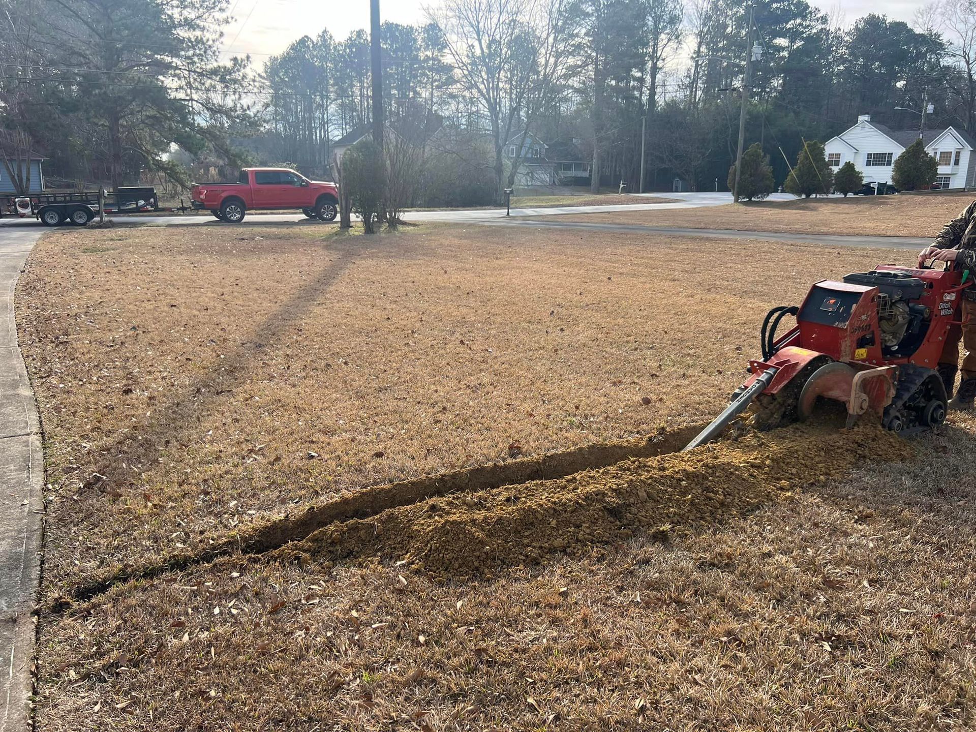 A red truck is driving down a dirt road next to a stump grinder.