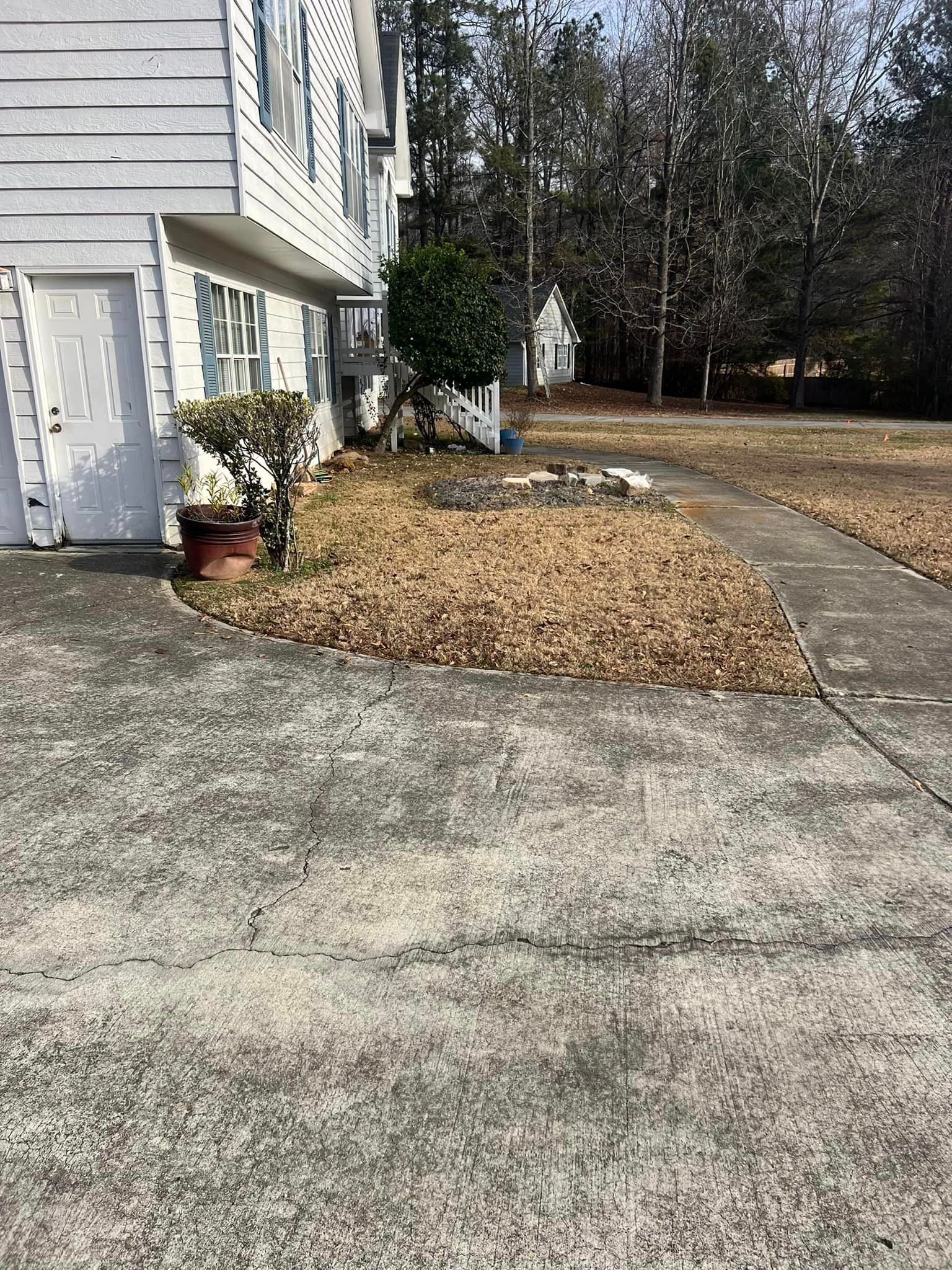 A concrete driveway leading to a house with trees in the background.