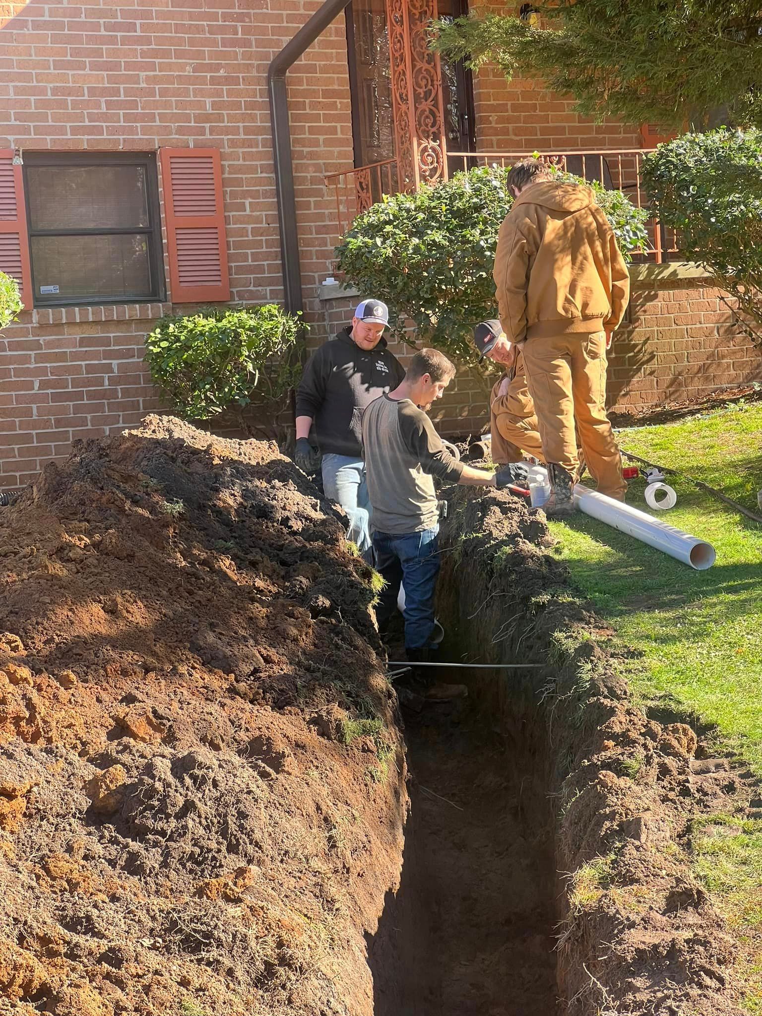 A group of people are digging a hole in the ground in front of a brick building.
