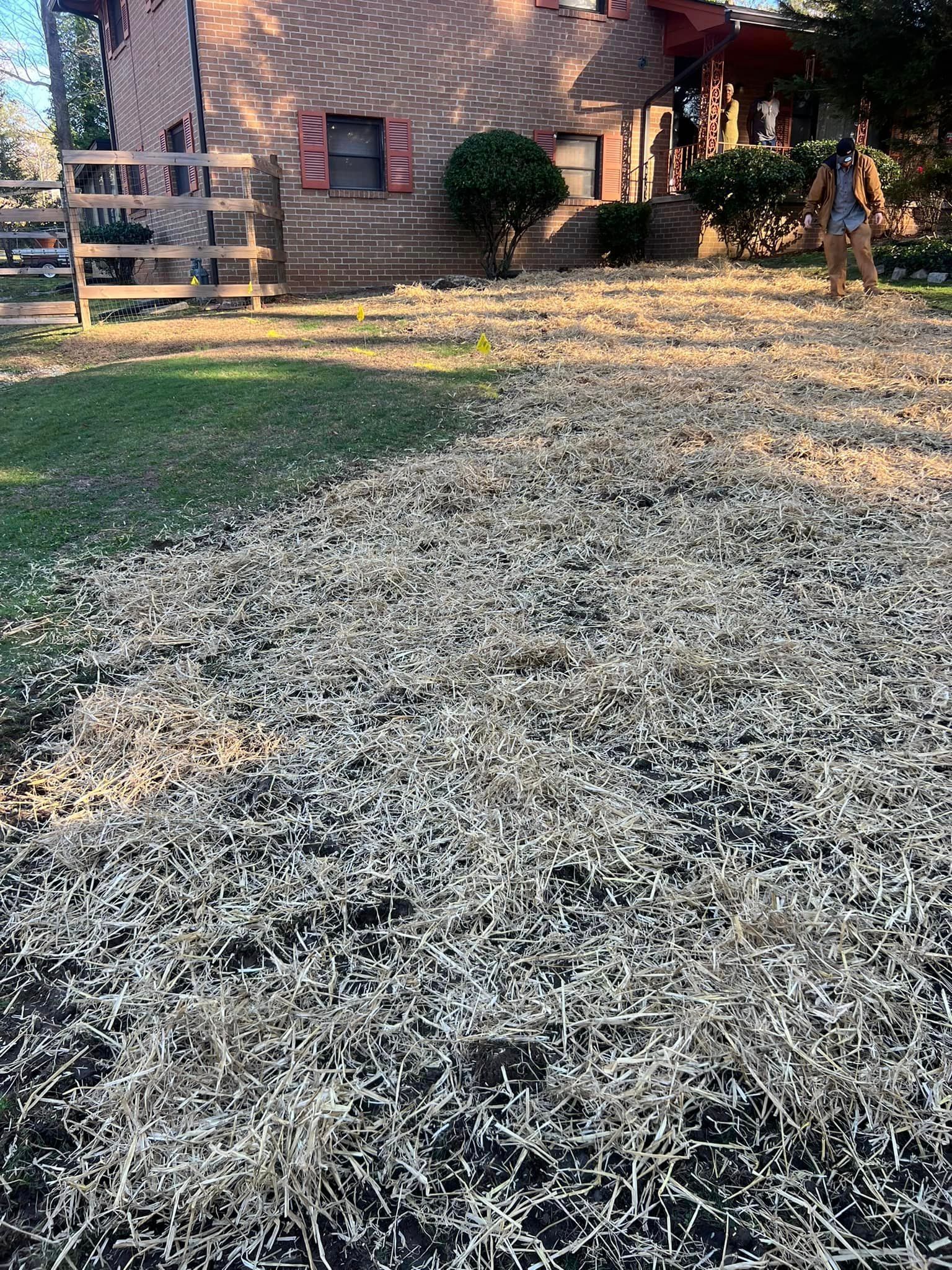 A woman is standing in a yard with a pile of hay in front of a house.