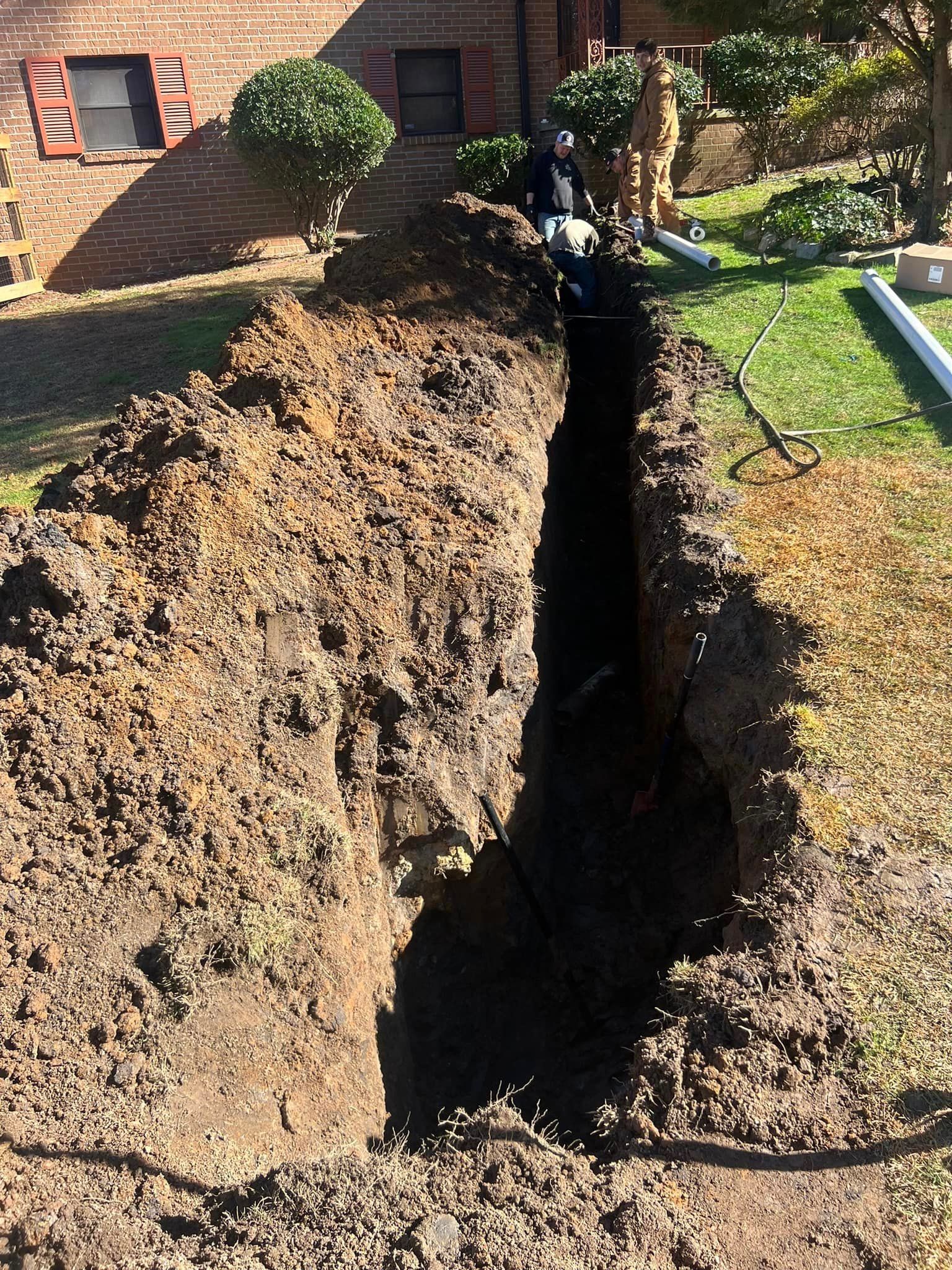 A large hole in the ground in front of a brick building.