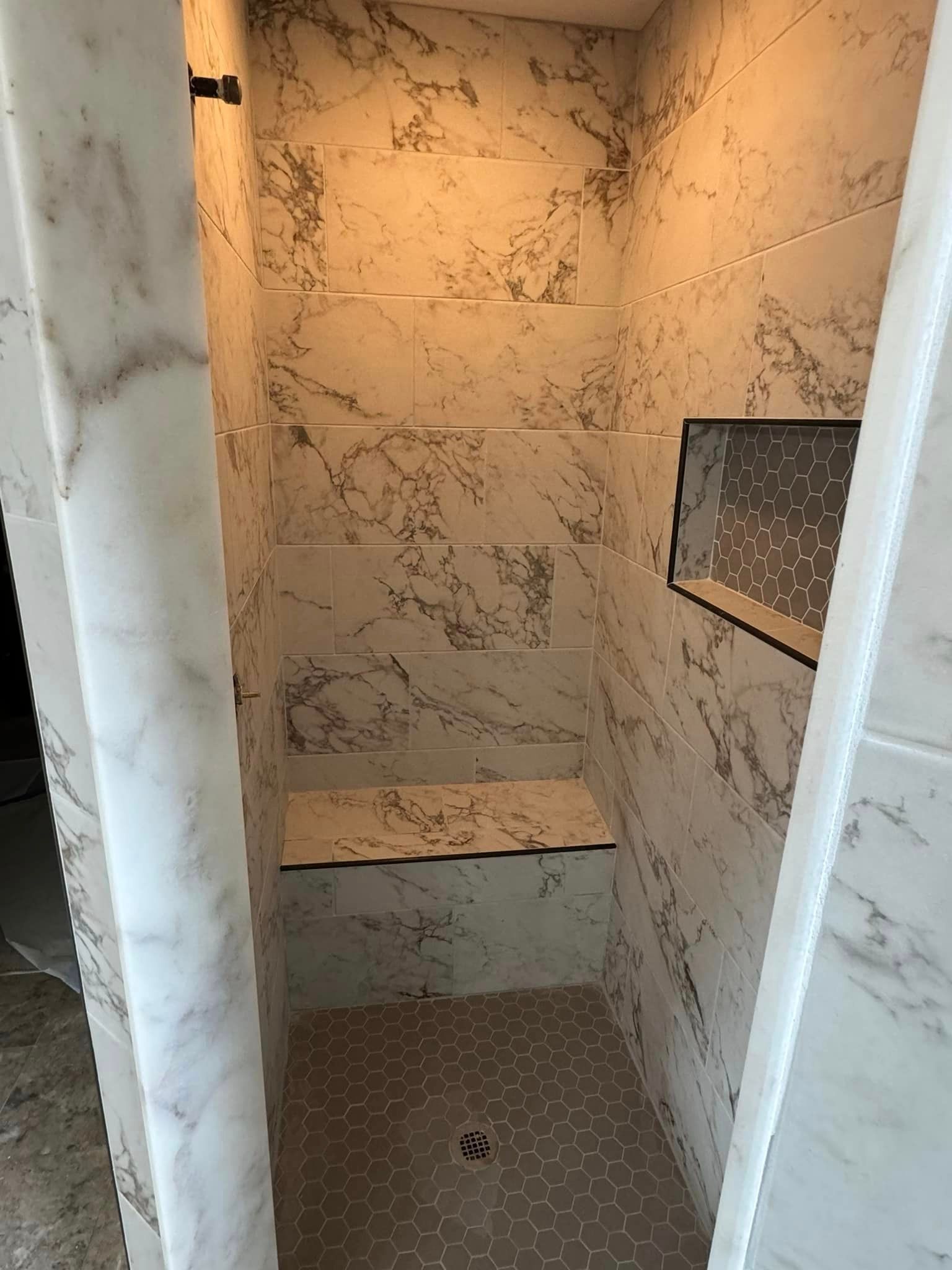 A shower stall with marble tiles and a bench.