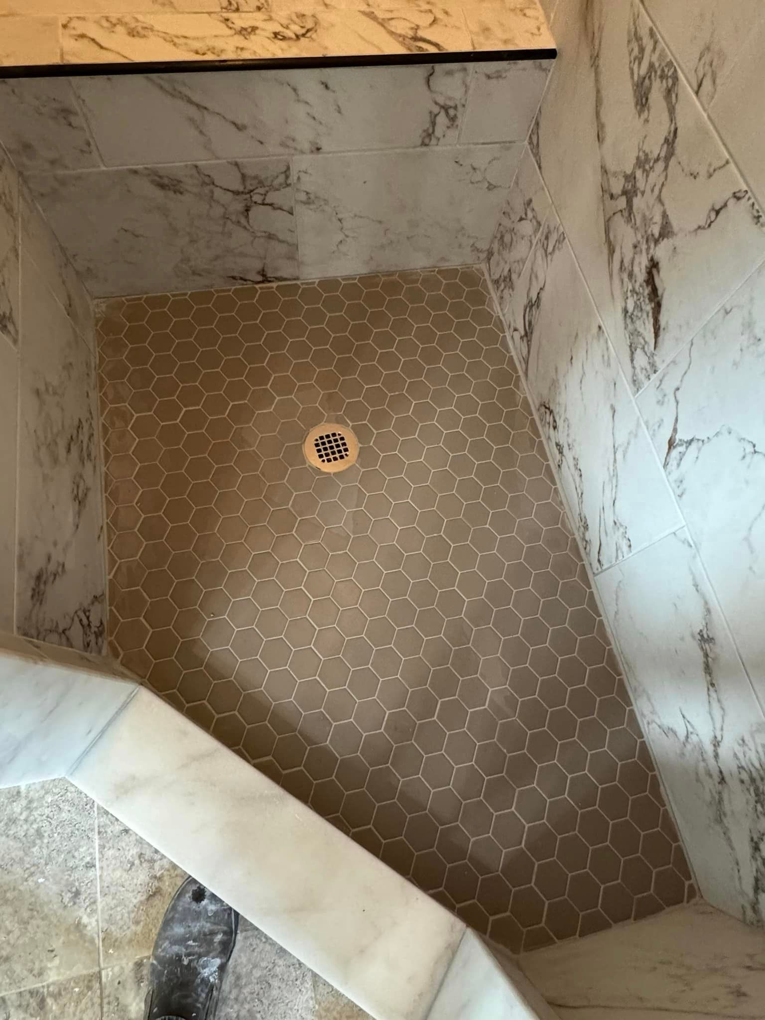 A shower stall with a tiled floor and a drain.