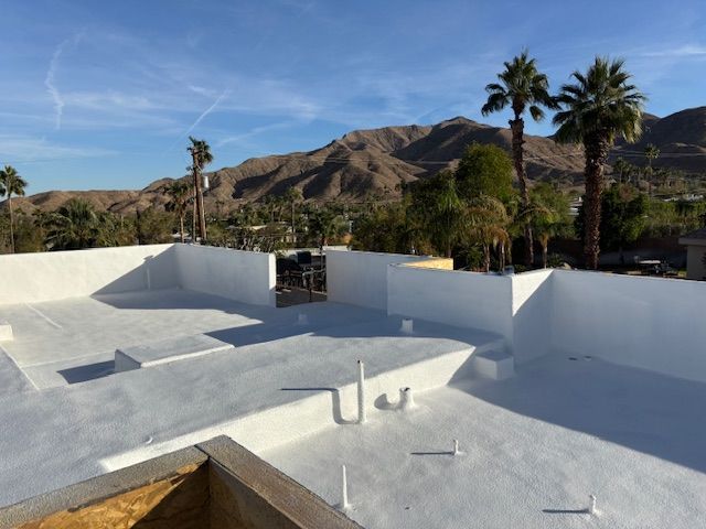 White flat roof with low walls, palms, and mountains in the background on a sunny day.