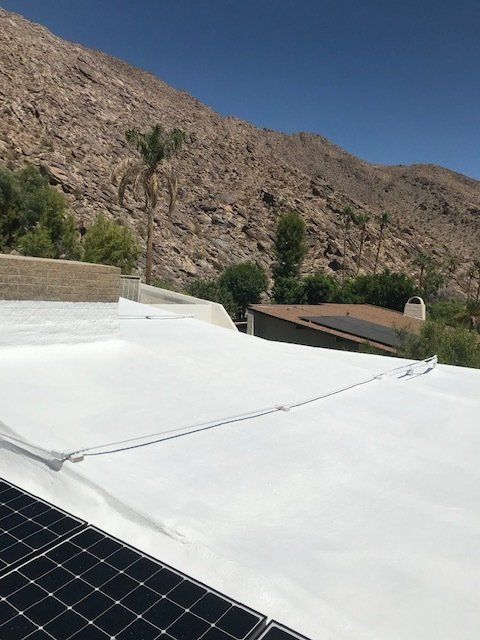White roof with solar panel in front, mountain backdrop, sunny day.