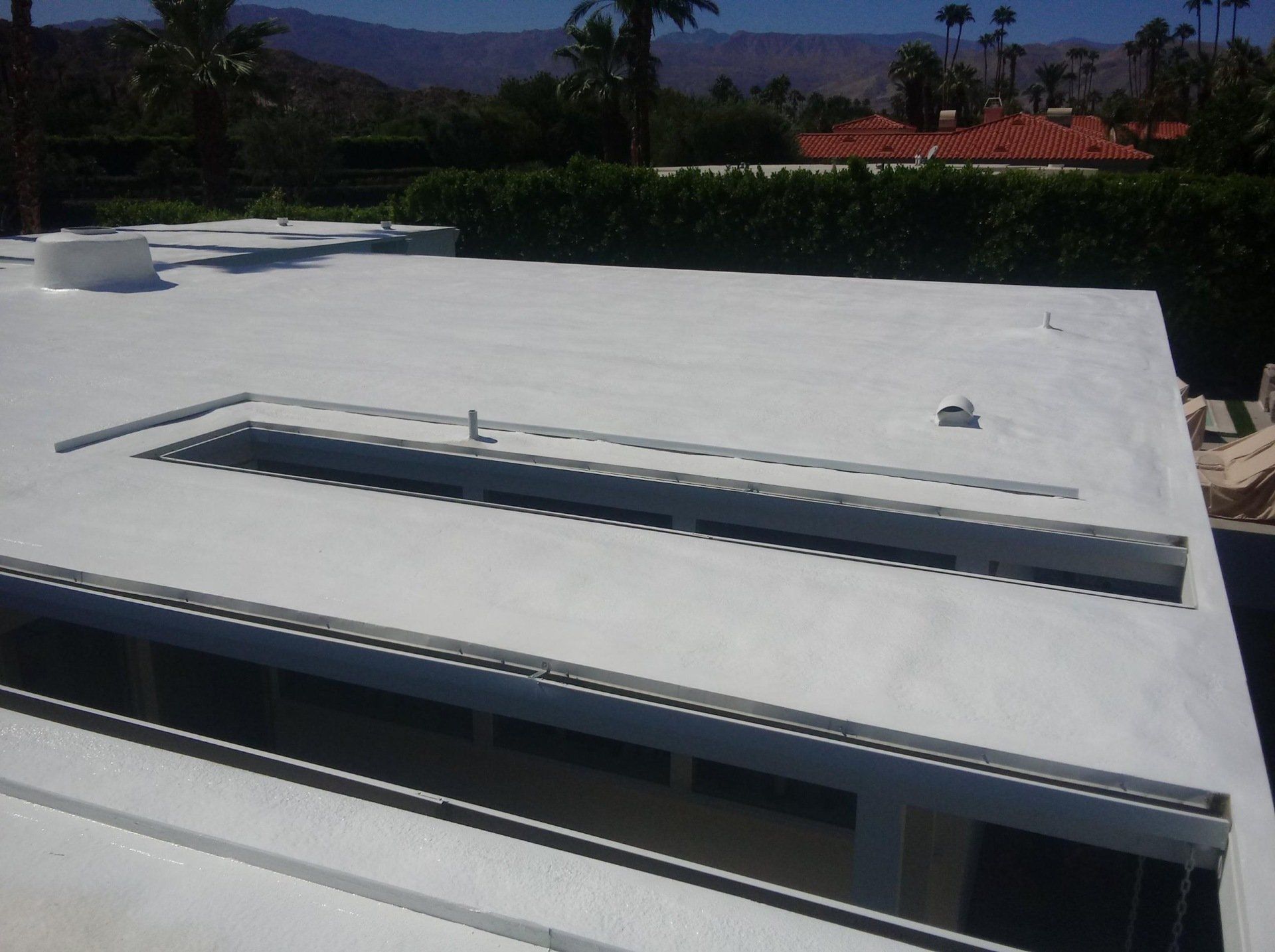 White flat roof with a rectangular opening, sunlight, and palm trees visible in the background.