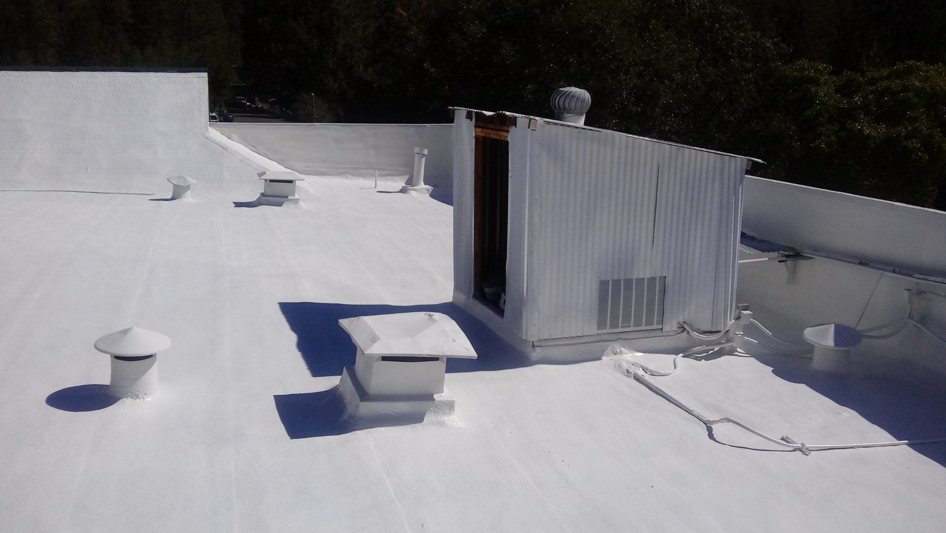 White-coated flat roof with vents, a utility enclosure, and the sunny background.