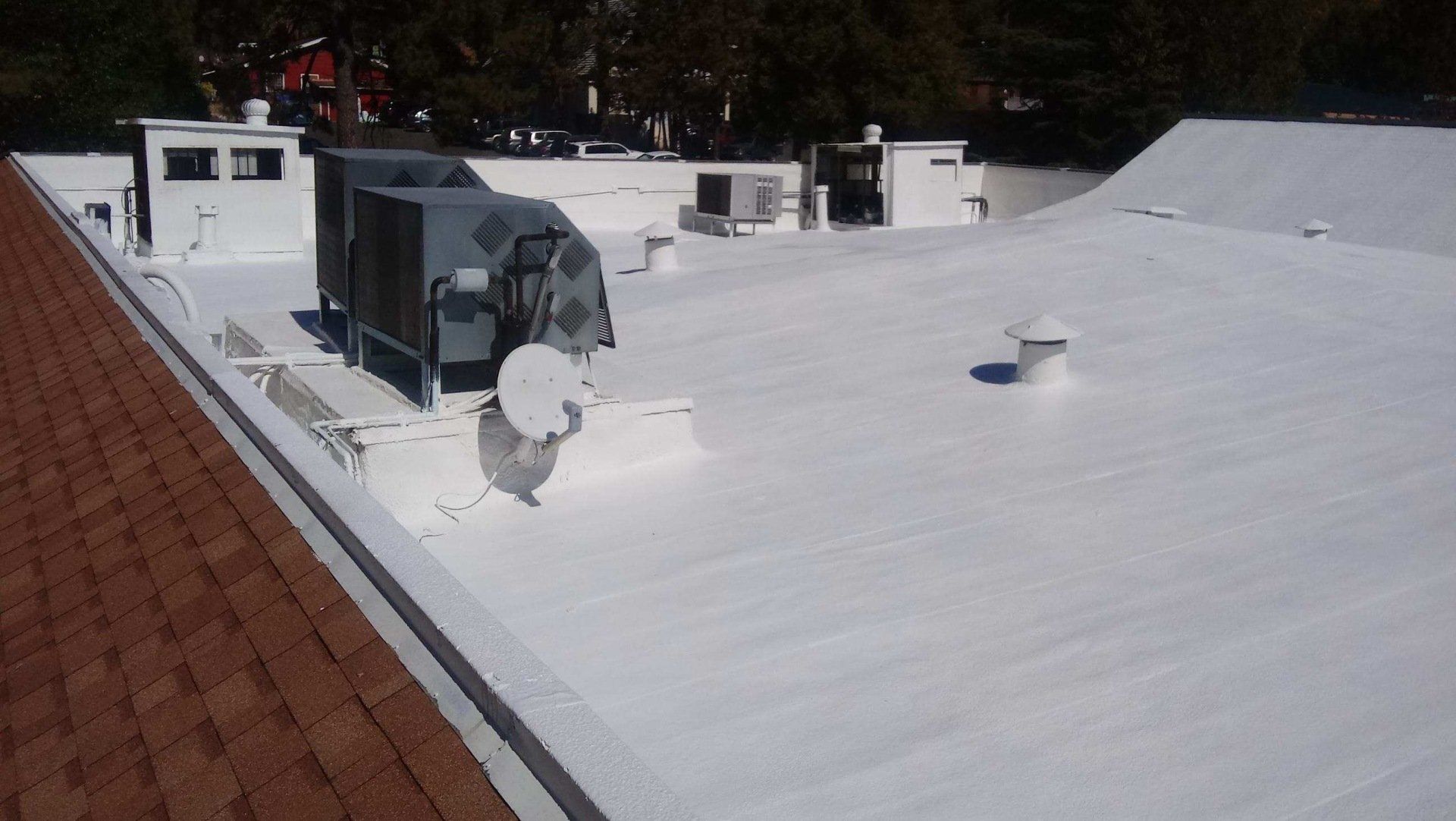 A white commercial flat roof with HVAC units and vents; adjacent to a brown shingle roof.