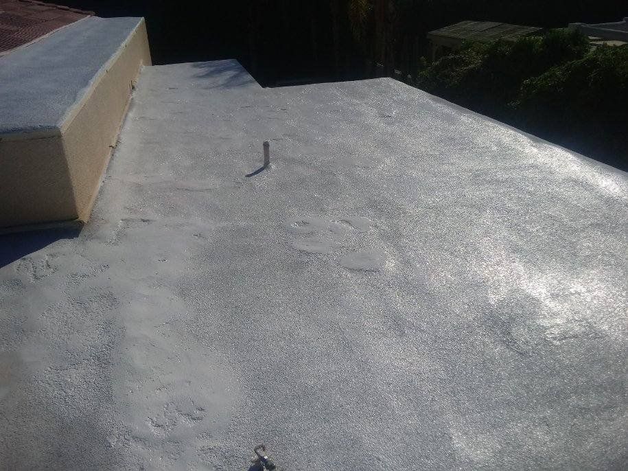 Flat, gray rooftop with a raised section on the left side, in bright daylight. A small metal object rises from the surface.