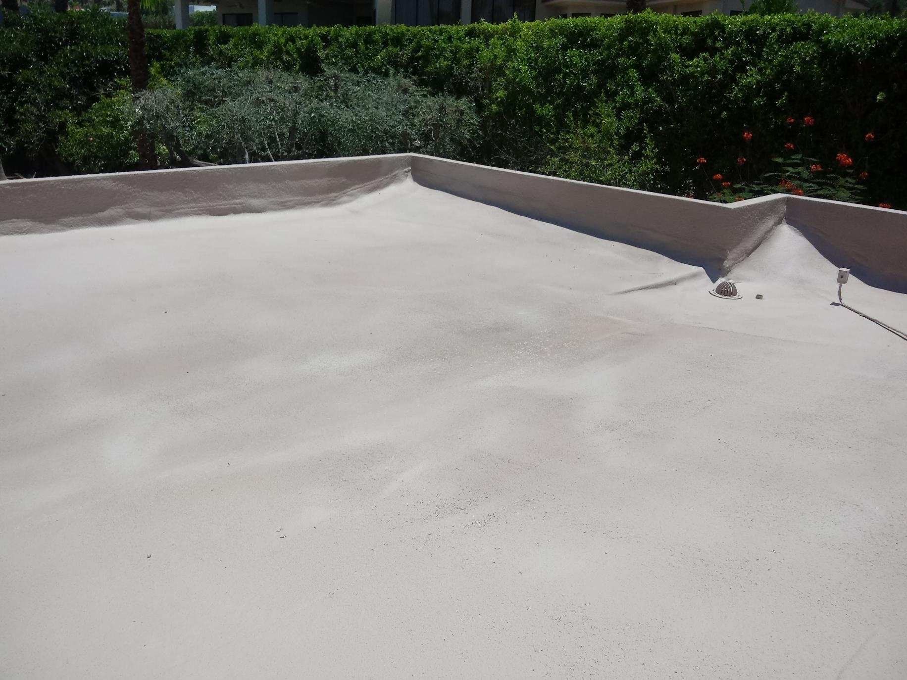 A light-colored, flat rooftop with rounded edges, against a backdrop of green bushes and trees.