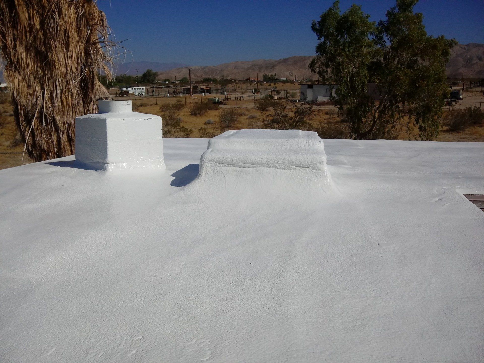 White-coated roof with two white structures, set against a desert landscape and clear blue sky.