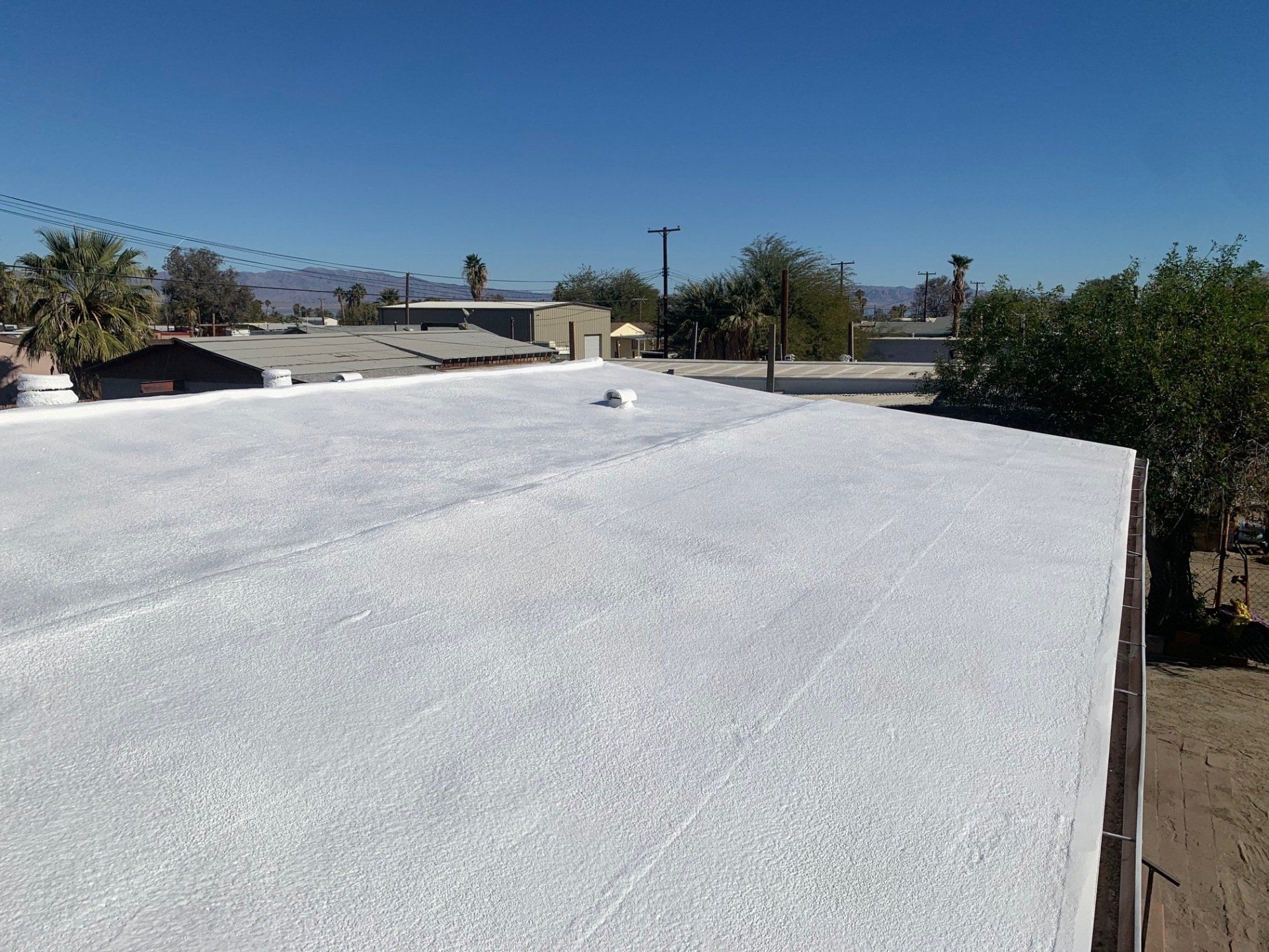 White coated roof under a clear blue sky, with buildings and sparse trees in the background.