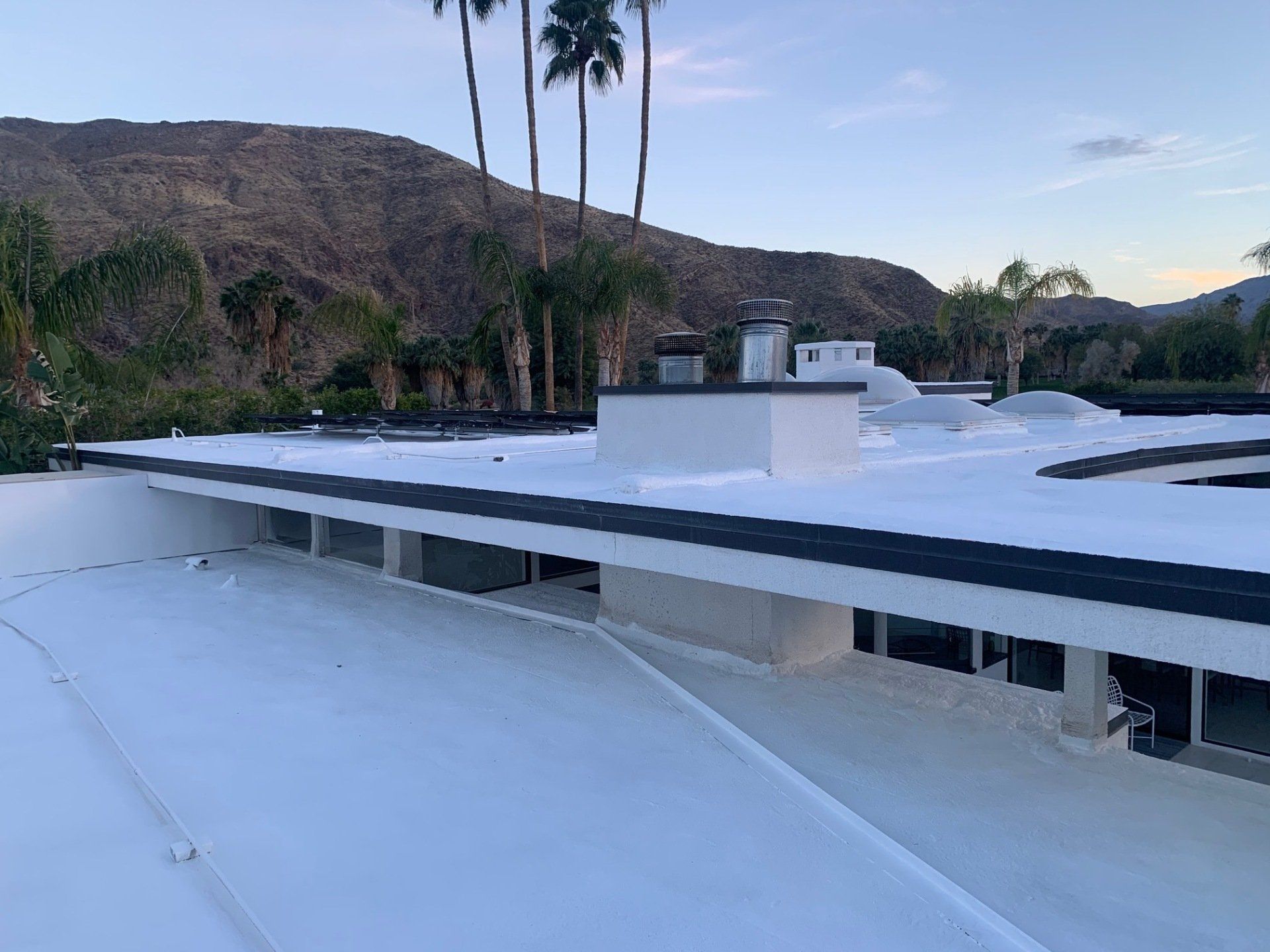 White flat roof of a building with a mountain backdrop. Palm trees are visible.