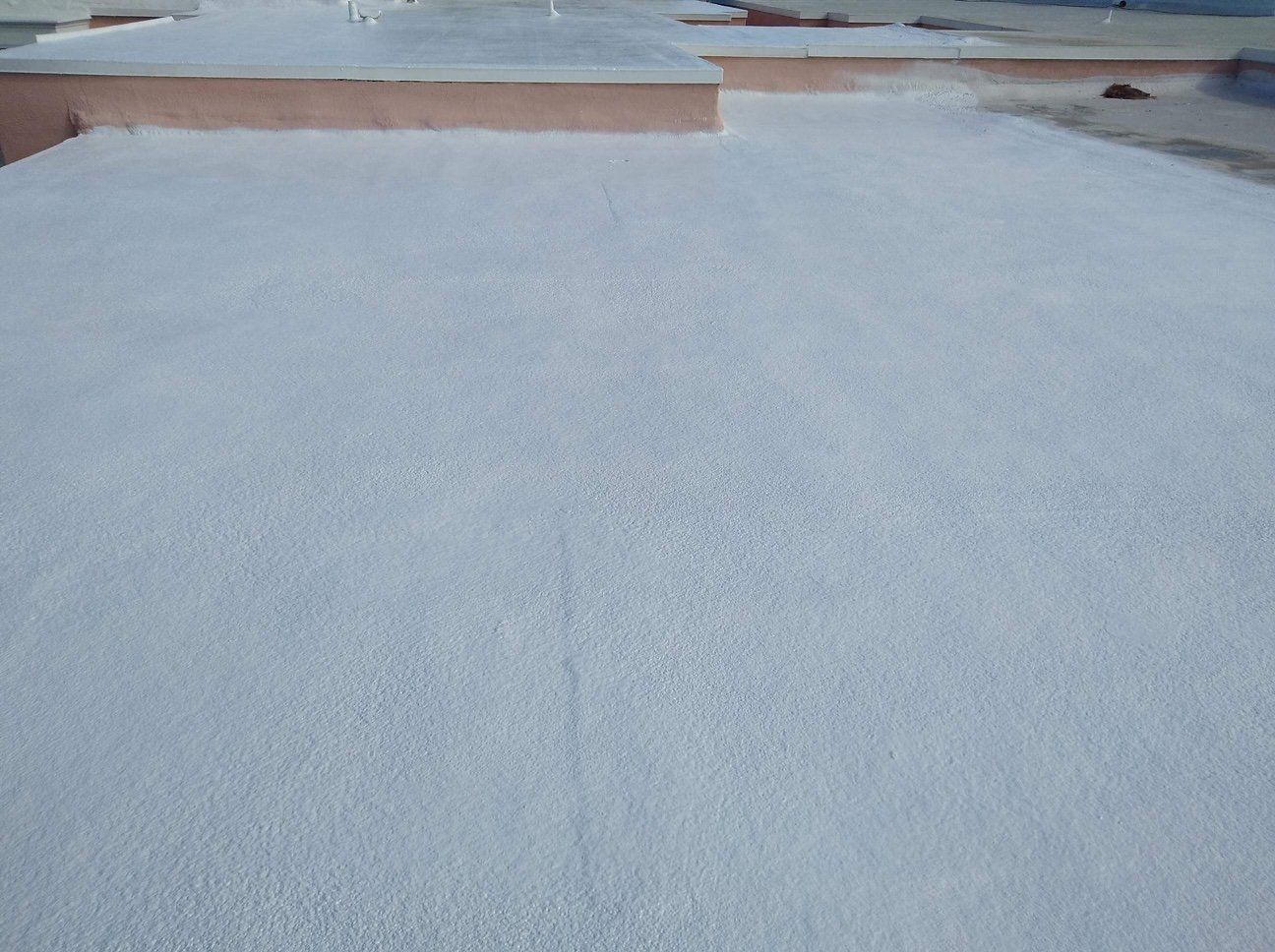 White coated rooftop, possibly for waterproofing. The roof has a slightly textured surface with a concrete border in the background.