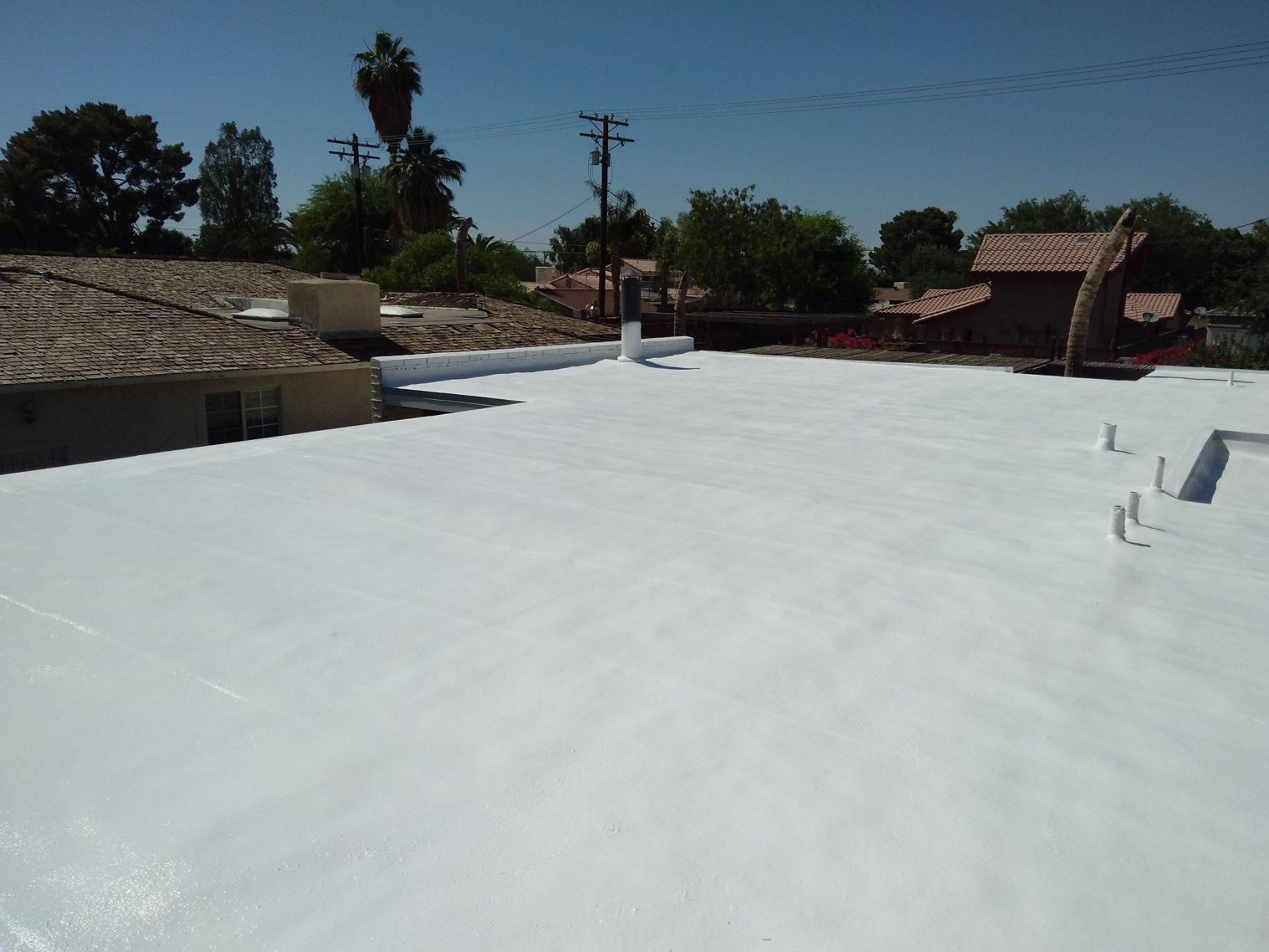 A bright white, flat roof on a sunny day, surrounded by residential buildings and trees under a clear blue sky.