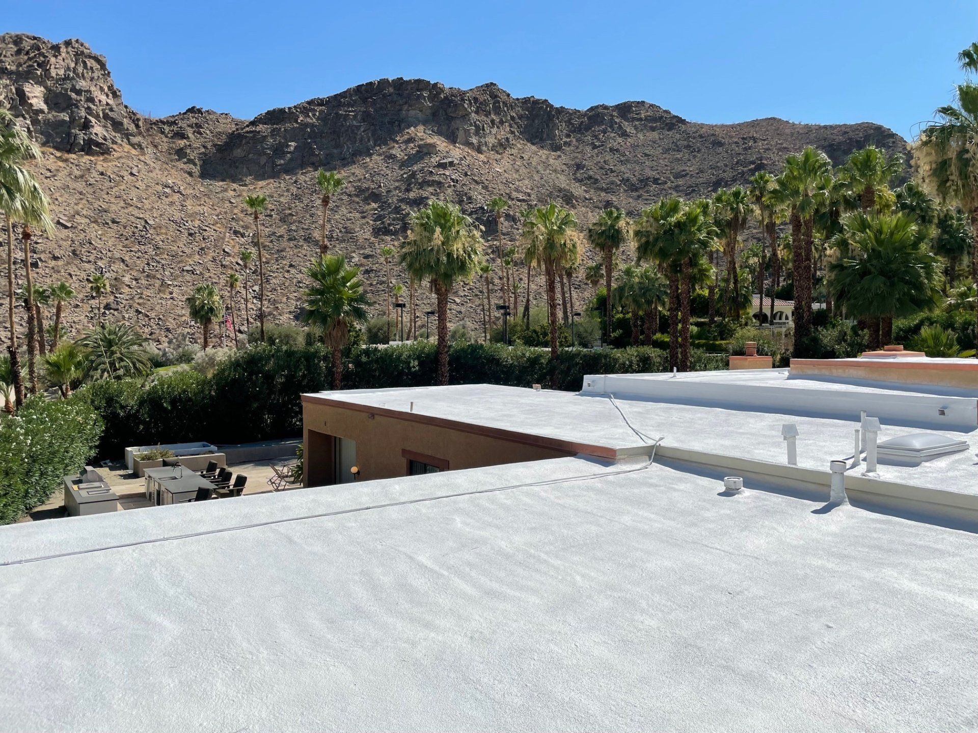 A white rooftop with a view of a rocky mountain range, palm trees, and lush greenery under a bright sky.