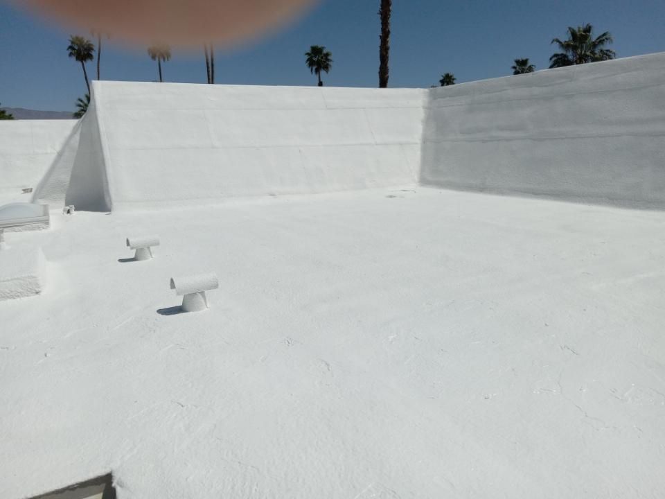 White flat roof with white walls, vents, and palm trees in the background under a blue sky.