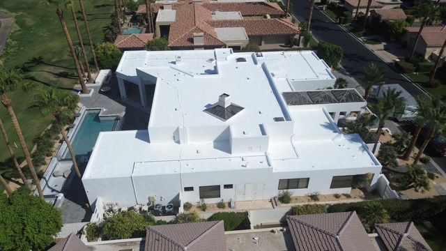 Aerial view of a white, modern house with a flat roof, a pool, and palm trees.